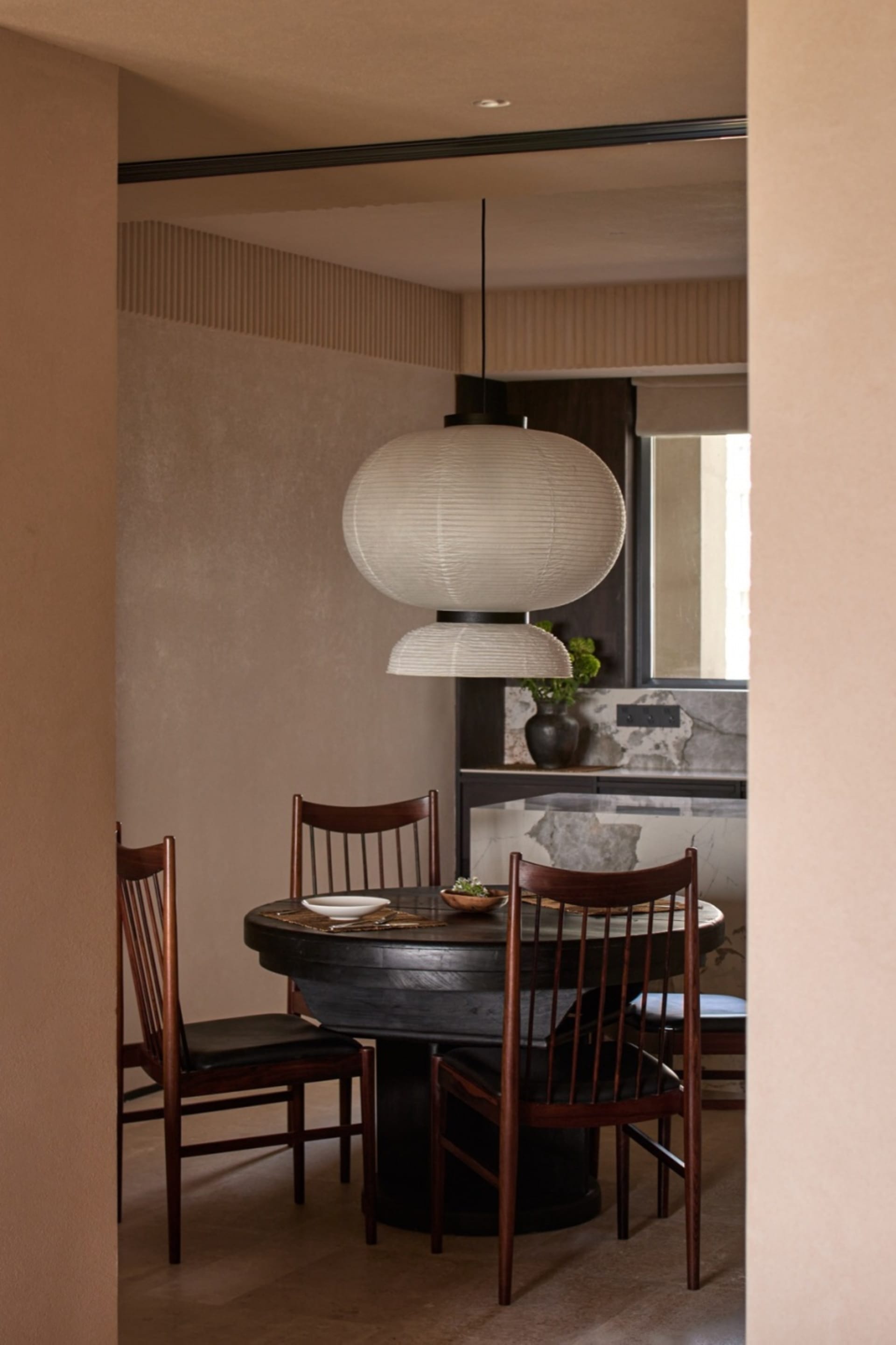 Modern minimalist dining room featuring a round wooden table with marble top, wooden chairs, and pendant lighting over the ta