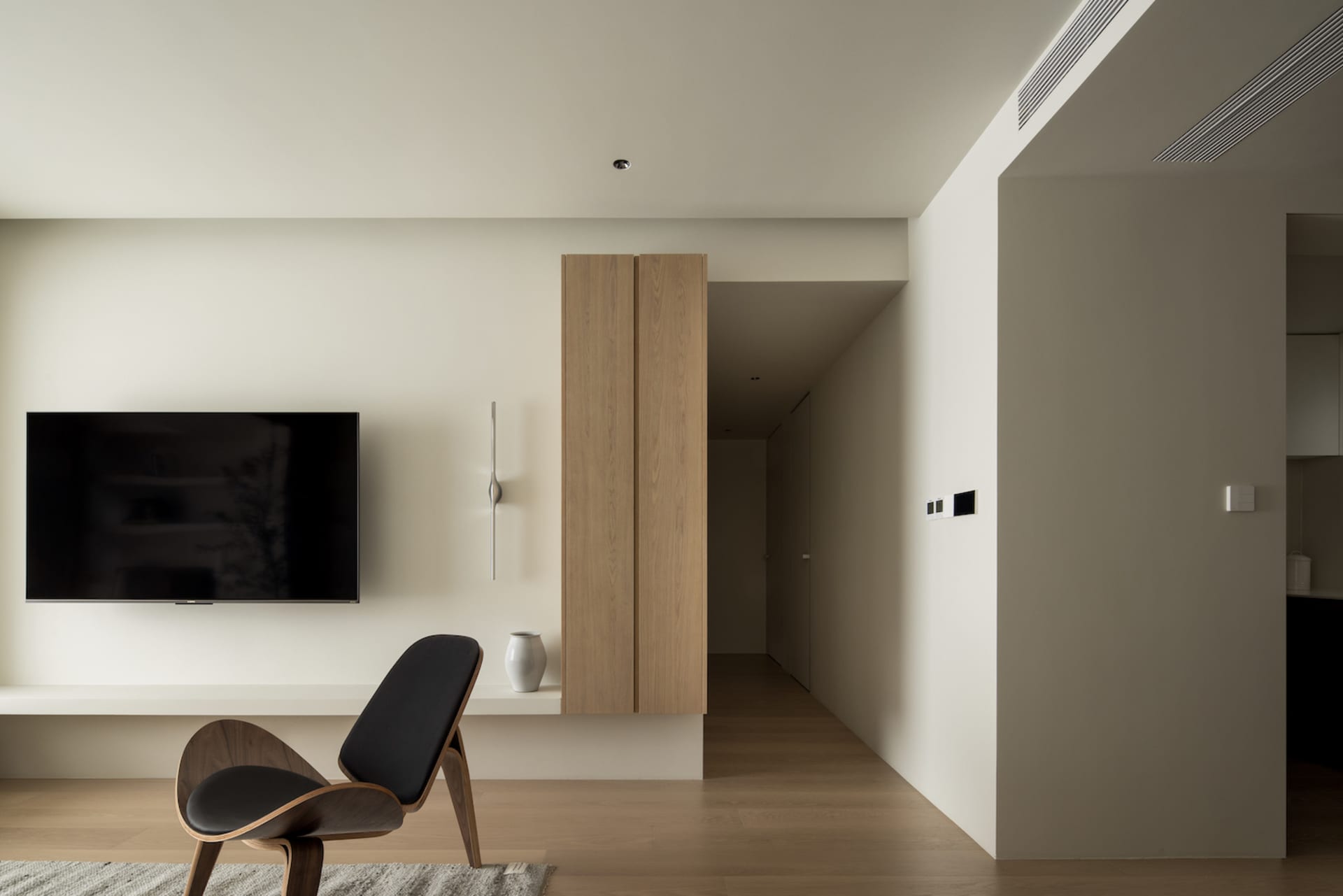 Modern, minimalist living room with a sleek, black armchair, wooden cabinet, and television.