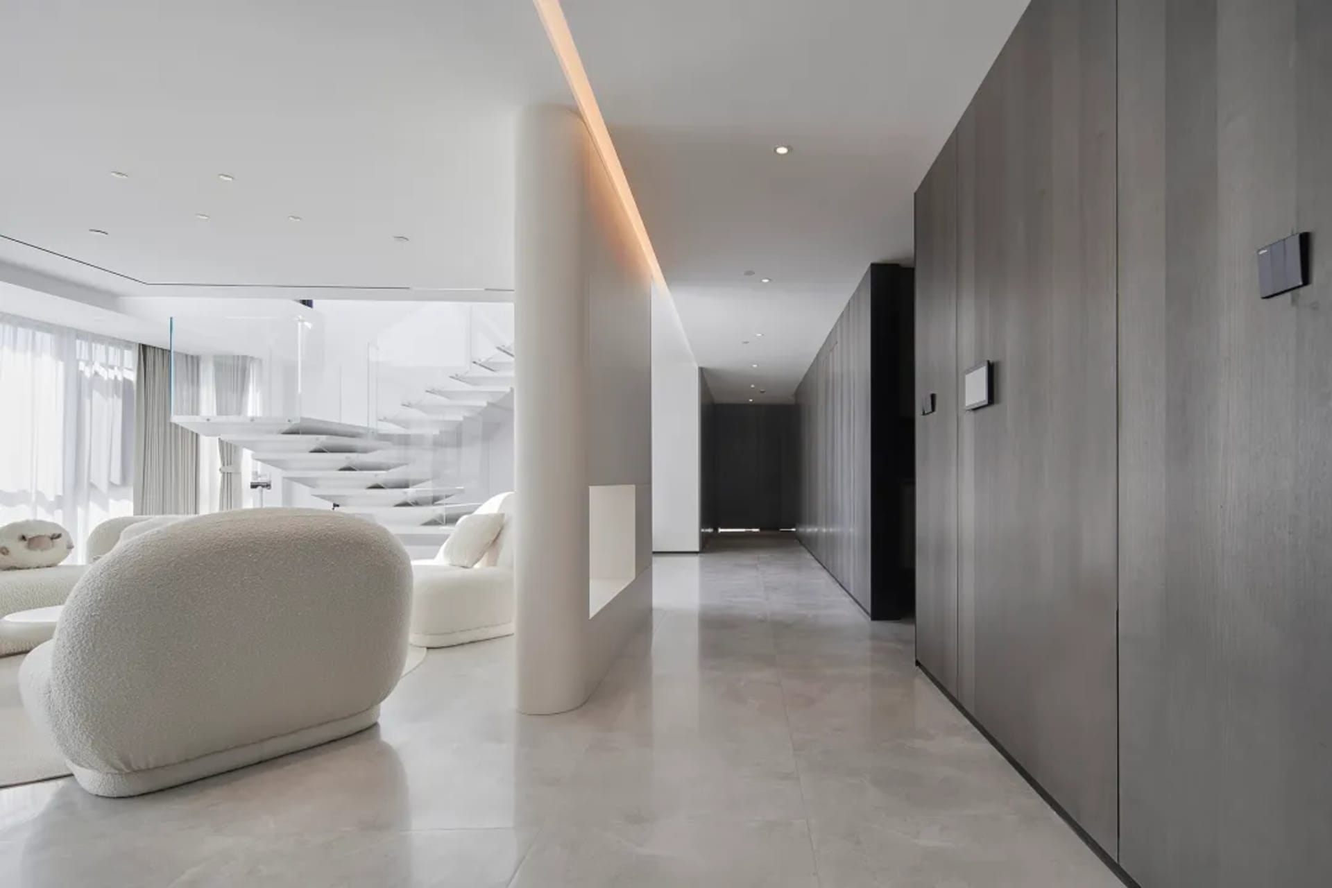 Modern living room with marble floating staircase and black wood cabinets on white marble floor.