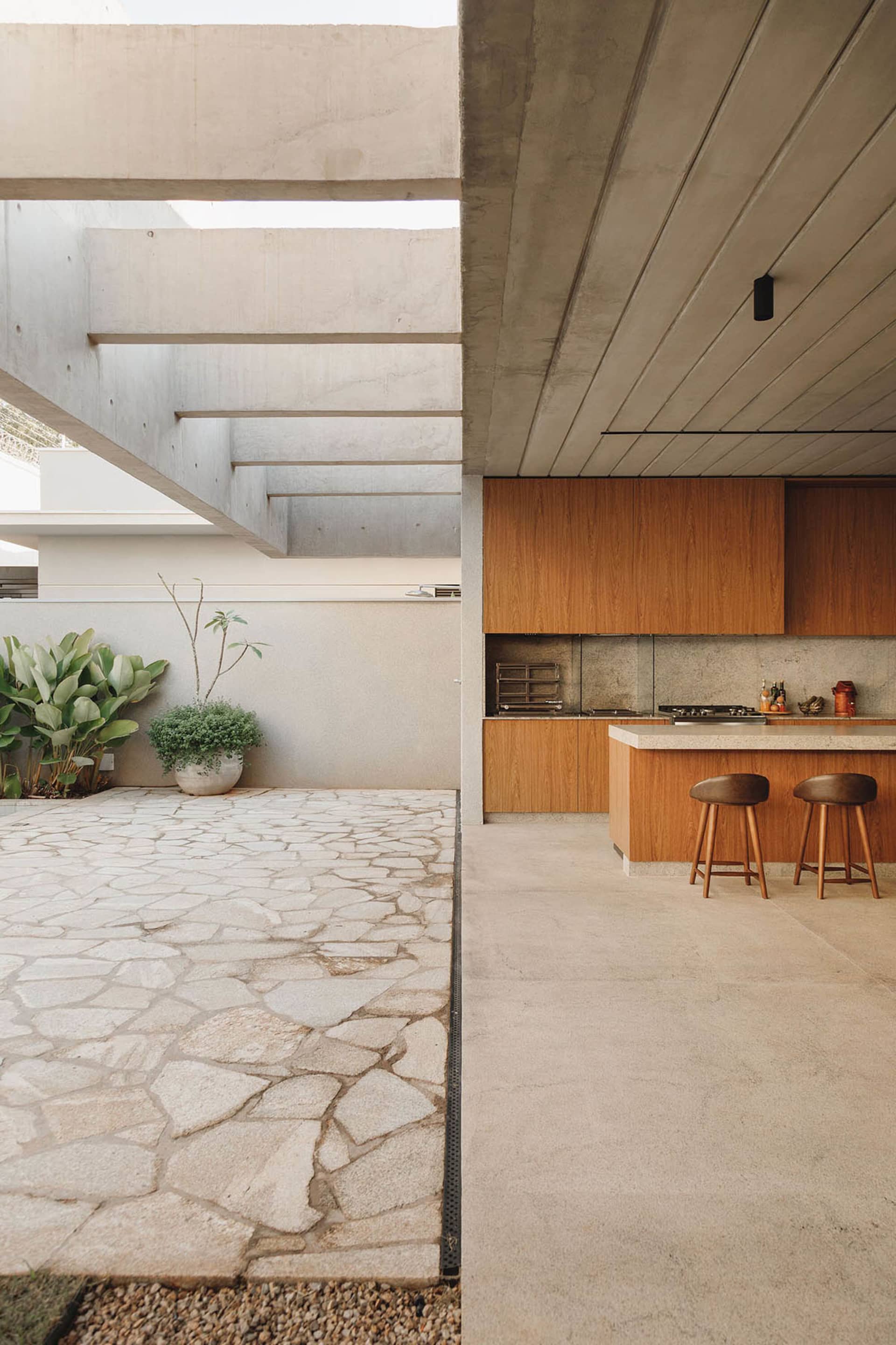 A modern patio featuring concrete flooring and a concrete staircase with greenery in the background.