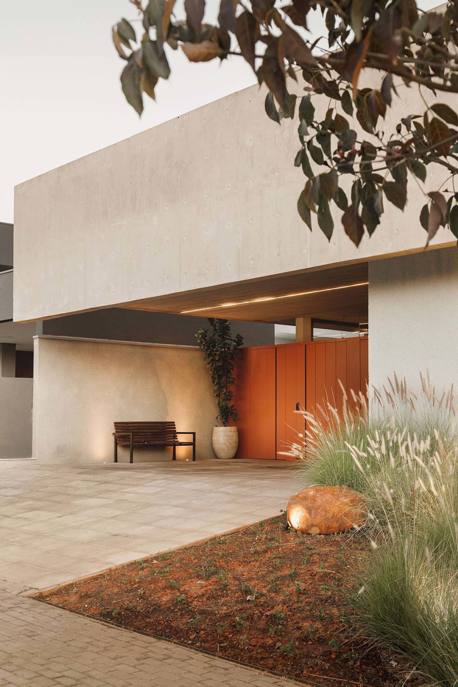 Concrete driveway with bench, potted plant, and garden in front of a modern house.