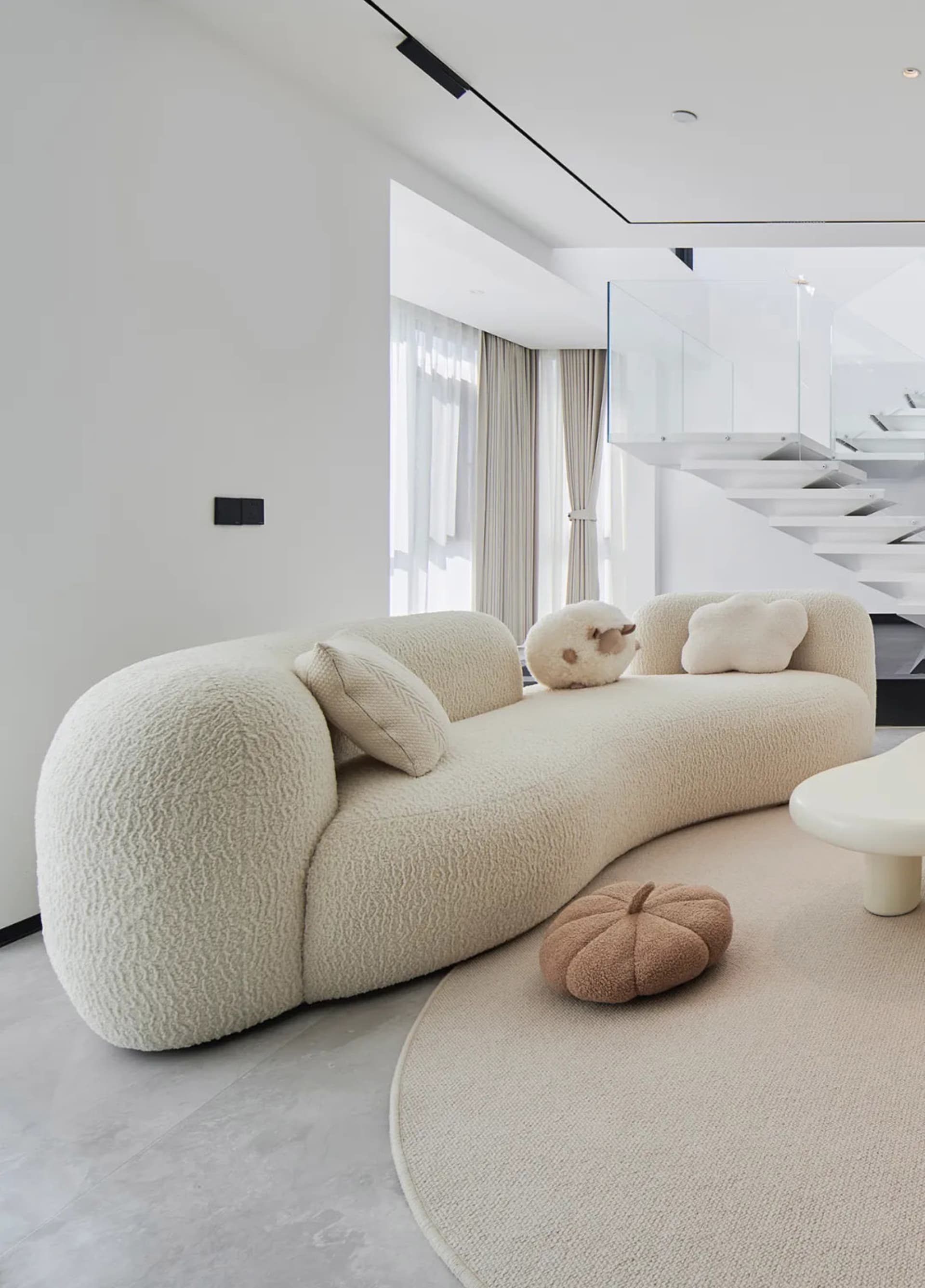 A modern living room with a textured sofa, round ottoman, and minimalistic design.