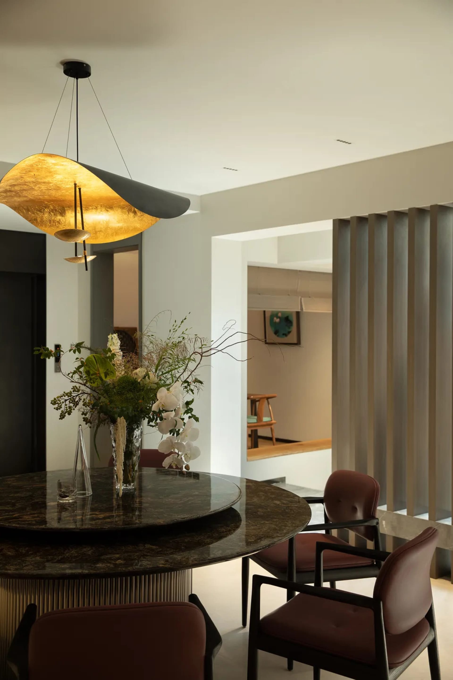 A modern dining room features a granite top dining table with a hanging pendant light and a floral centerpiece.