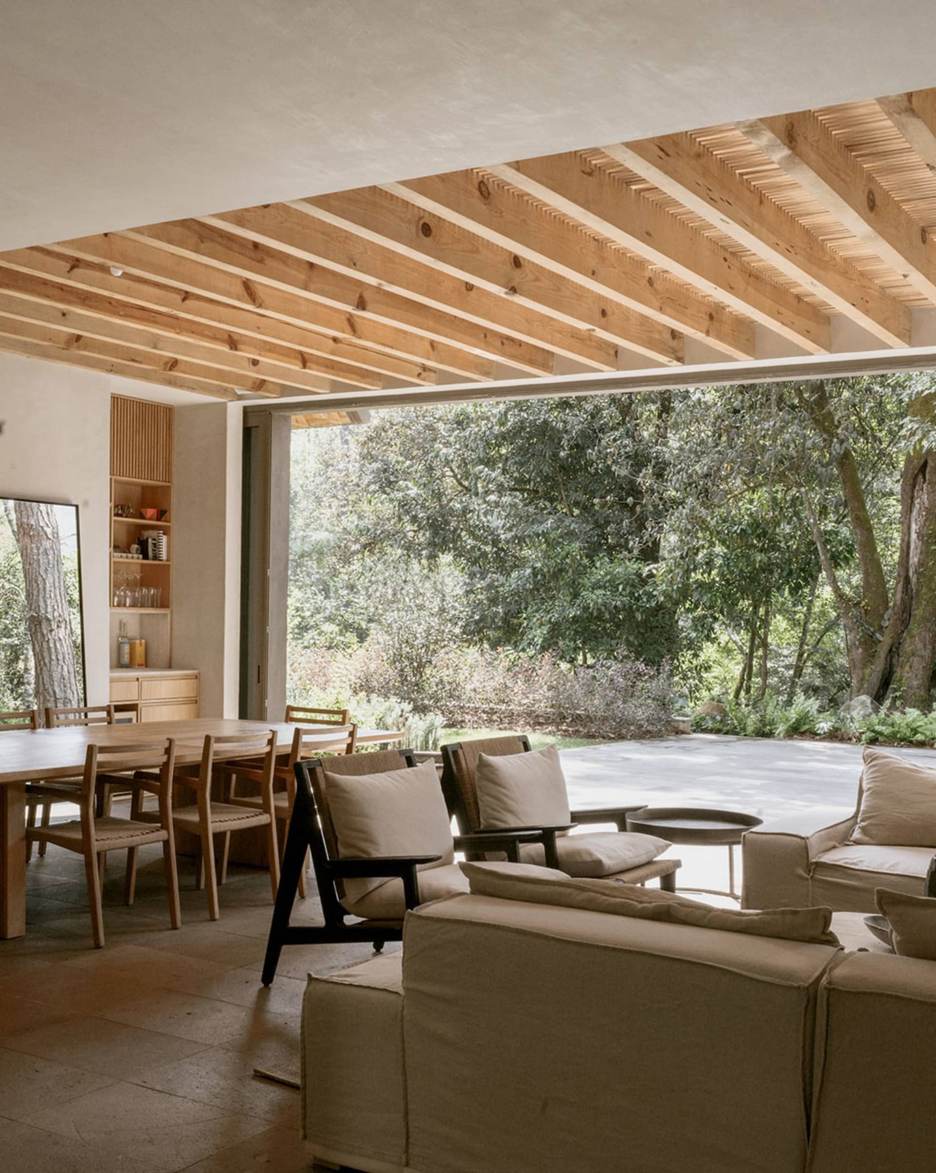 A minimalist living room featuring white concrete walls, large windows, and a comfortable seating area with light-colored fur