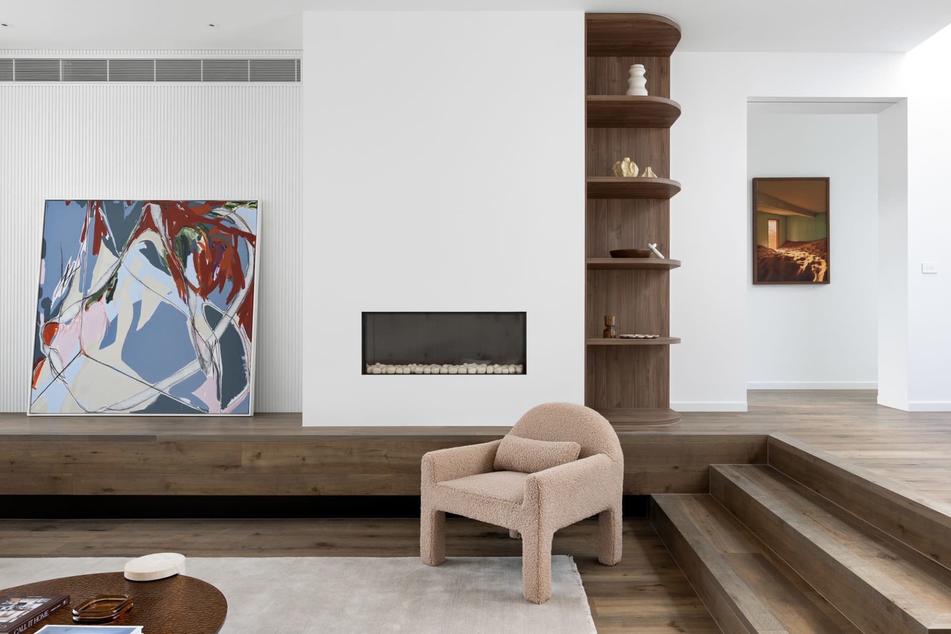 A minimalist living room featuring a wooden floor, a modern fireplace, and abstract art on the walls.