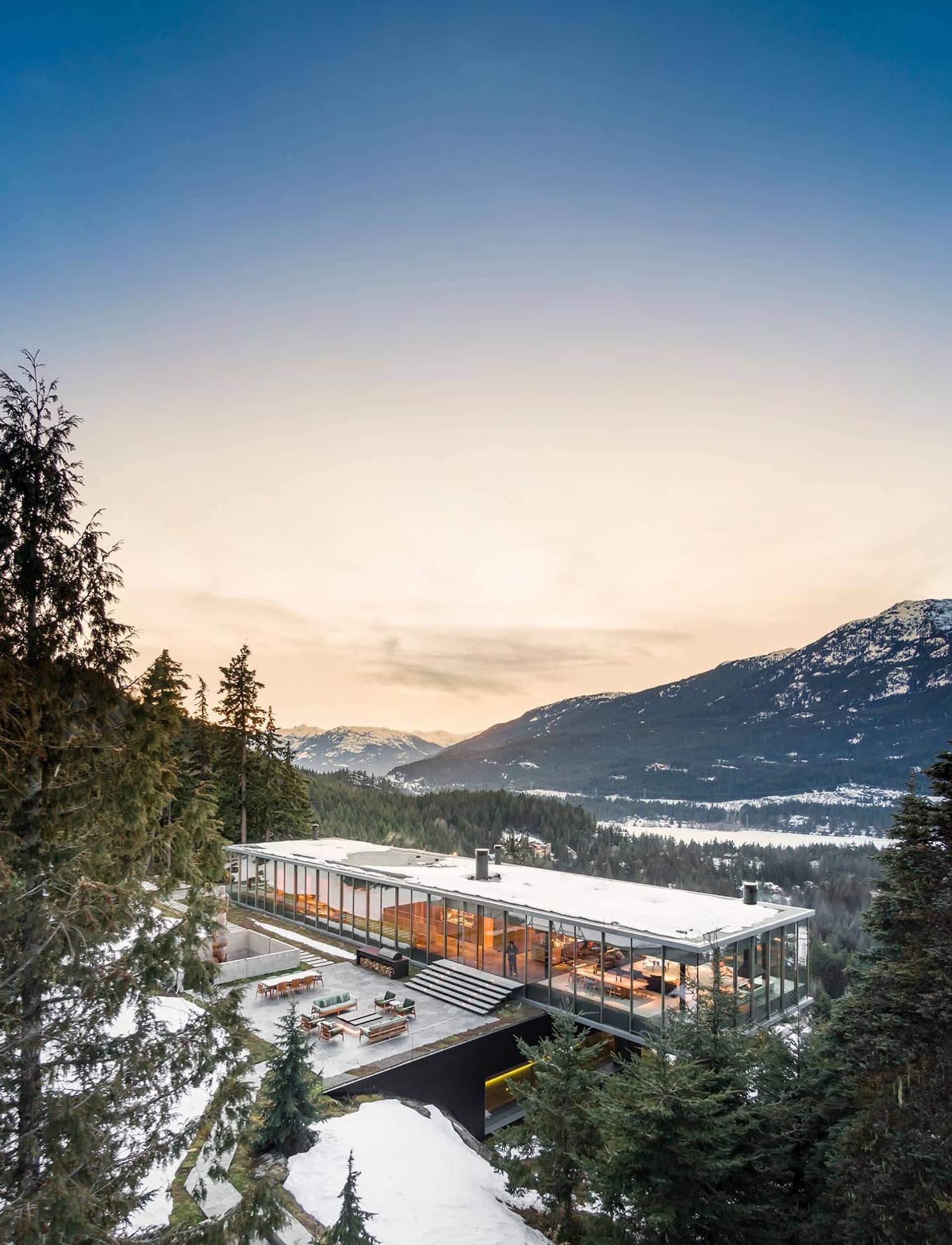 A modern residential building with large glass walls overlooking snowy mountains.