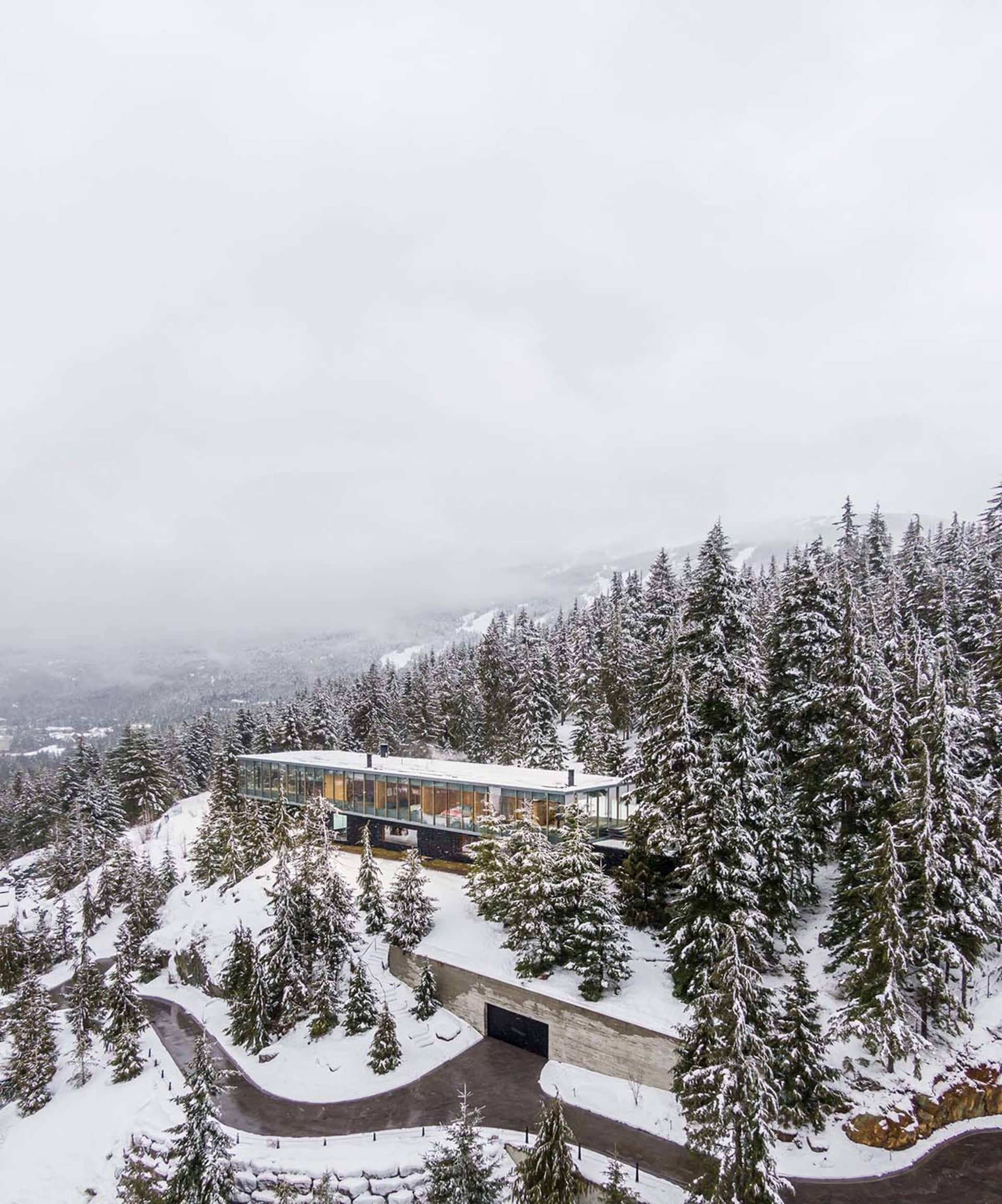 一座現代玻璃面住宅,坐落於覆雪的森林山坡上。
