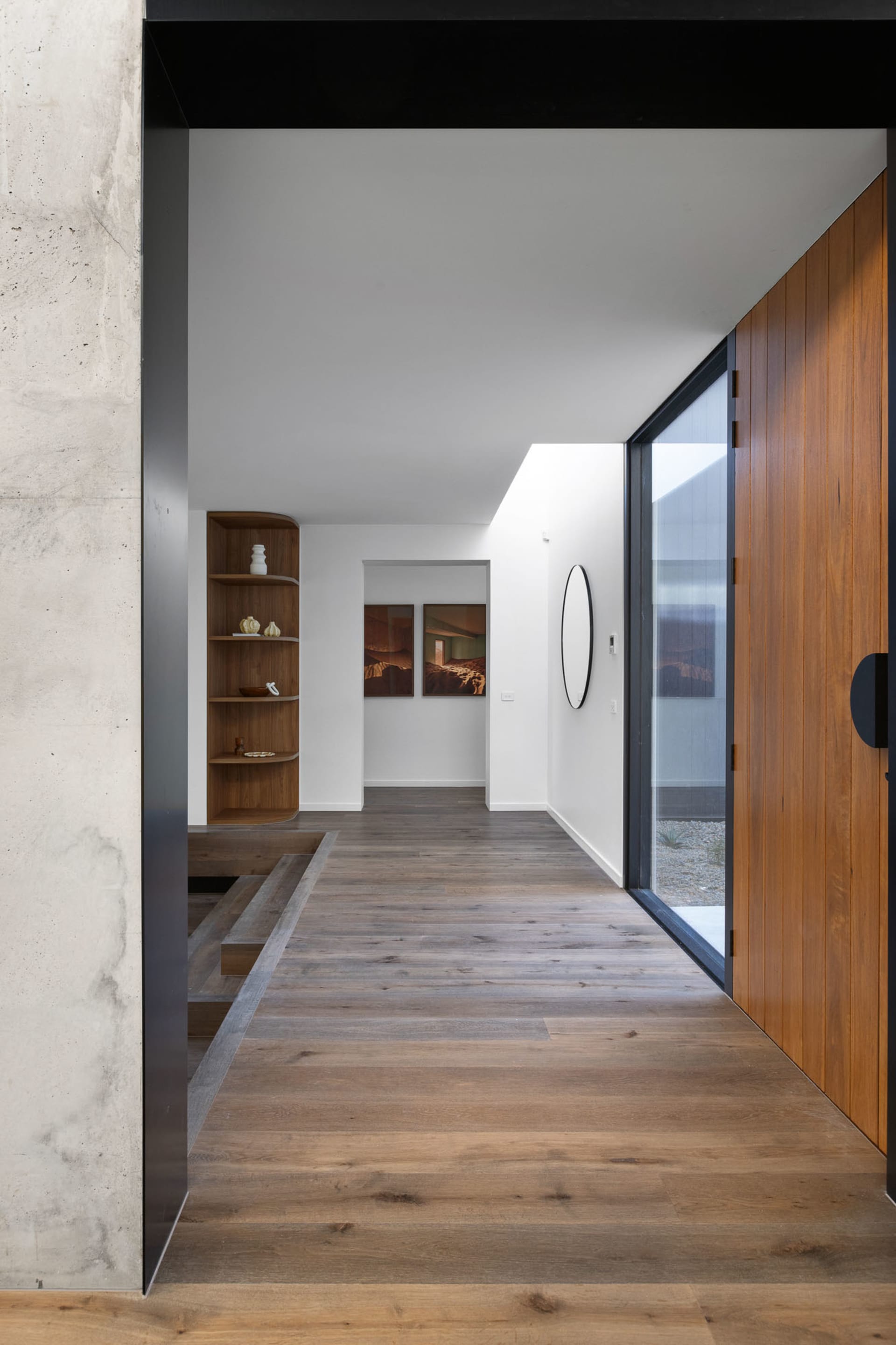 Modern entrance hall with wooden flooring, concrete walls, and glass elements.
