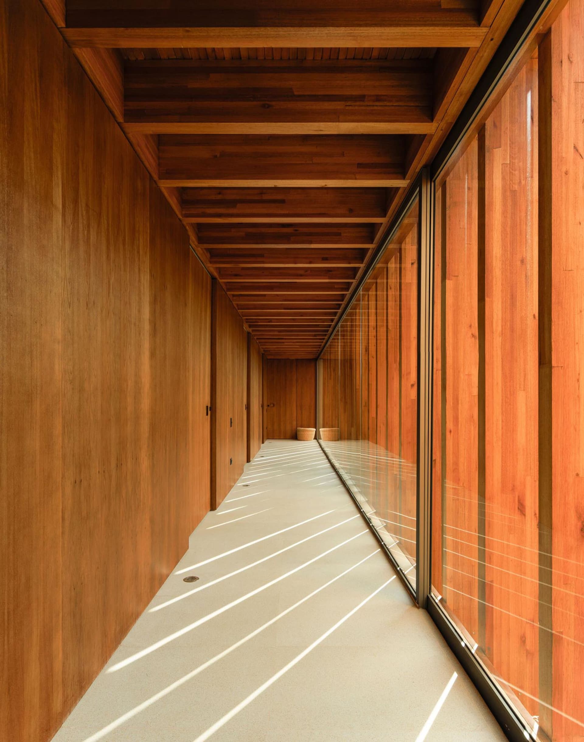 A minimalist corridor featuring wooden paneling and light streaming through windows.