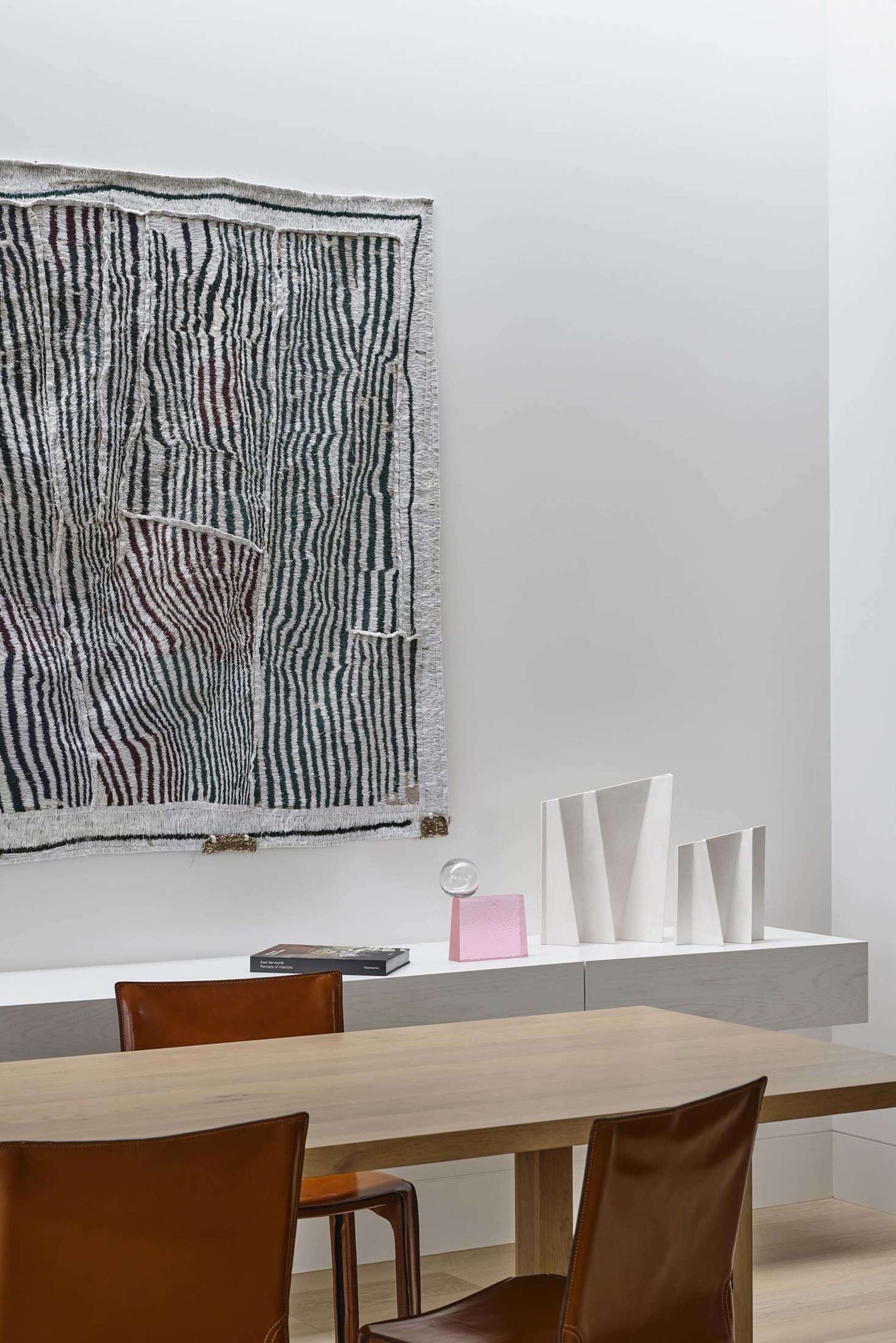 Modern dining room with wooden table and chairs, decorative rug, and abstract sculptures on a floating console.