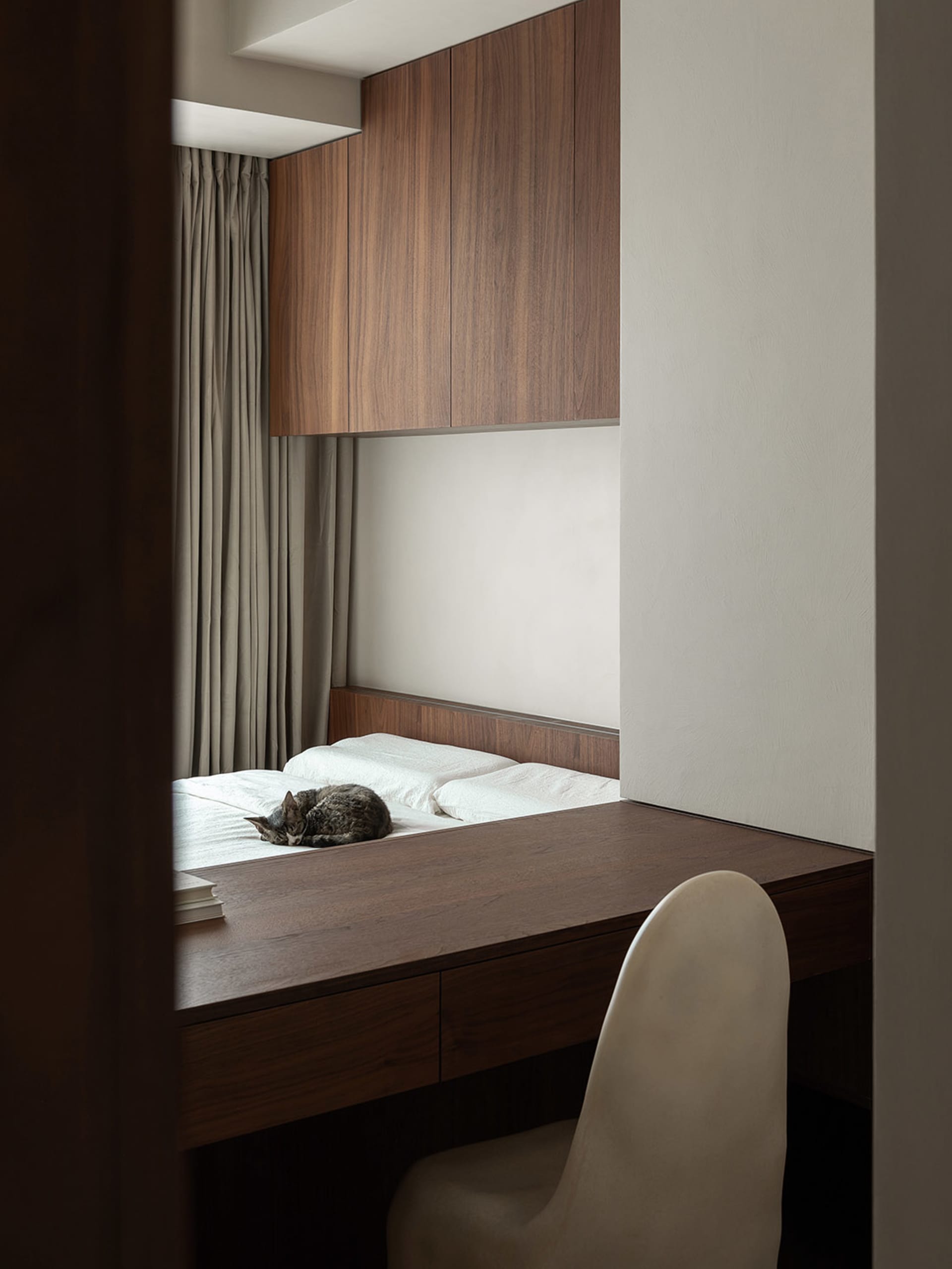 A minimalist bedroom with wooden furniture, including a bed with white bedding, a wooden desk, and a white chair.