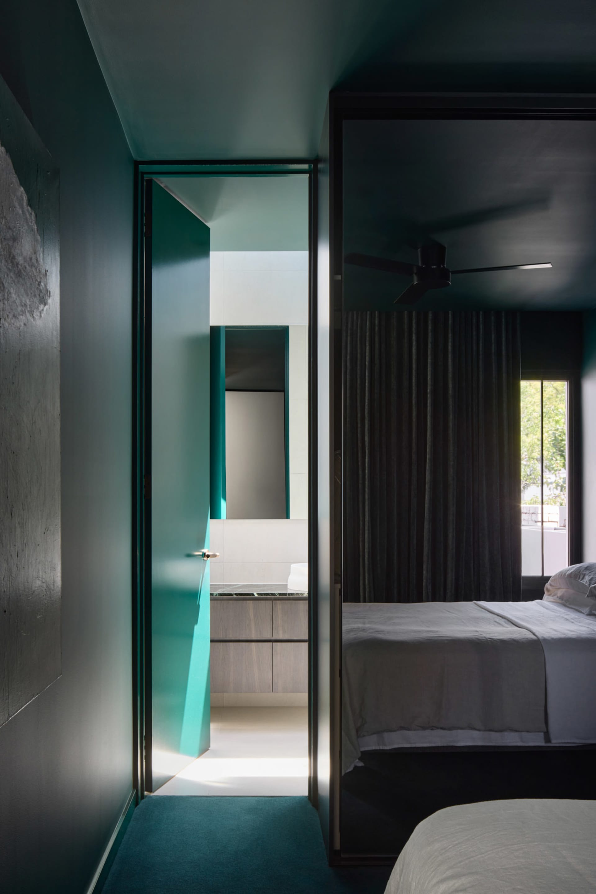 A modern bedroom featuring a glass door leading to an adjacent bathroom with white tiles and wooden cabinetry.