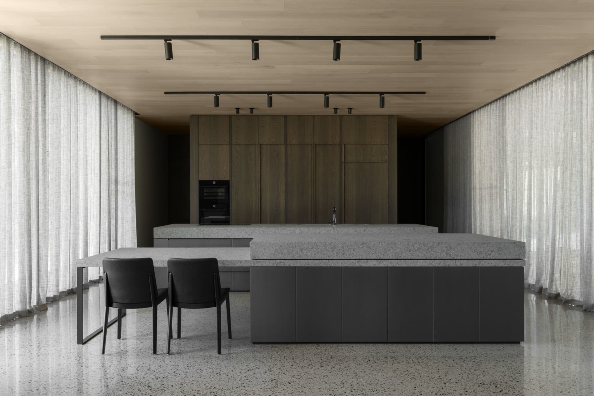 A minimalist kitchen with a granite countertop and black chairs.