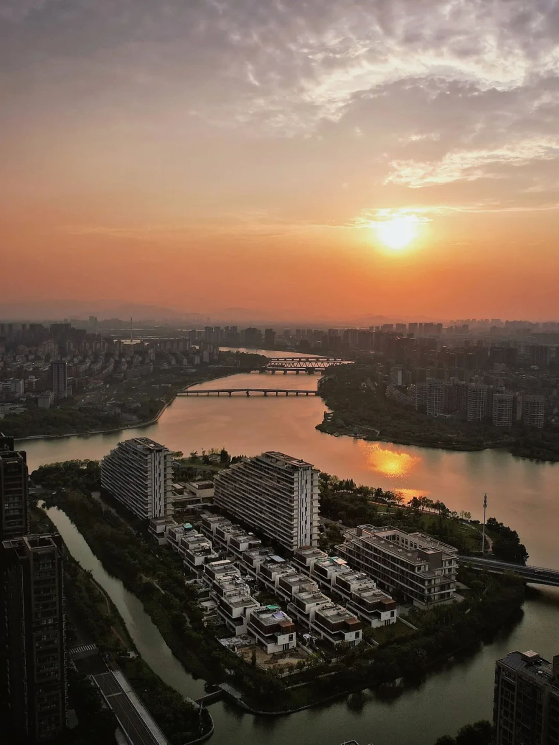 日落時分俯瞰城市景觀，河面橫跨多座橋樑，兩岸建築林立。