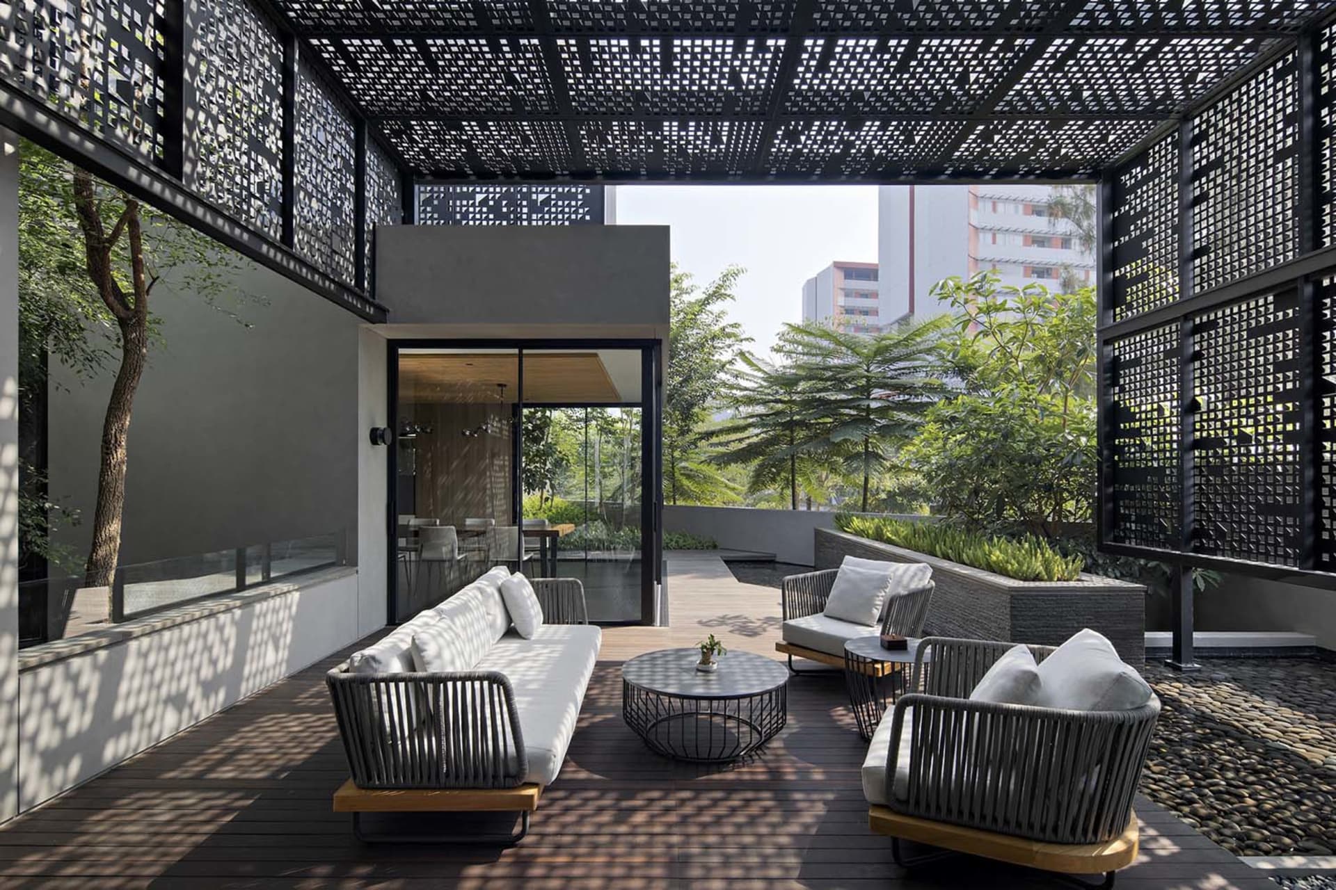 Modern urban living space featuring metal pergola, concrete walls, and wooden furniture.