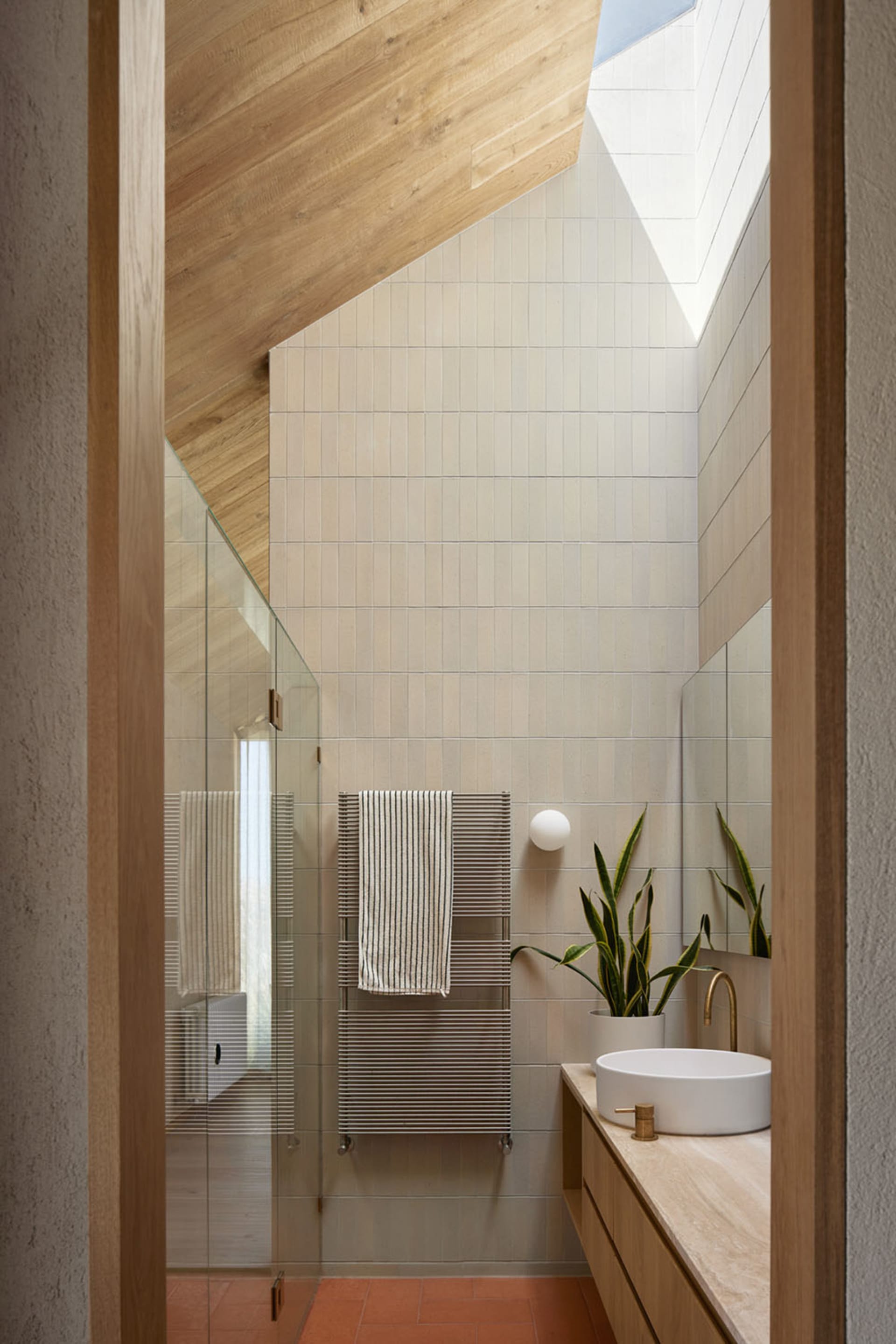 Modern bathroom with beige tiles, white sink, wooden accents, and a glass shower door.