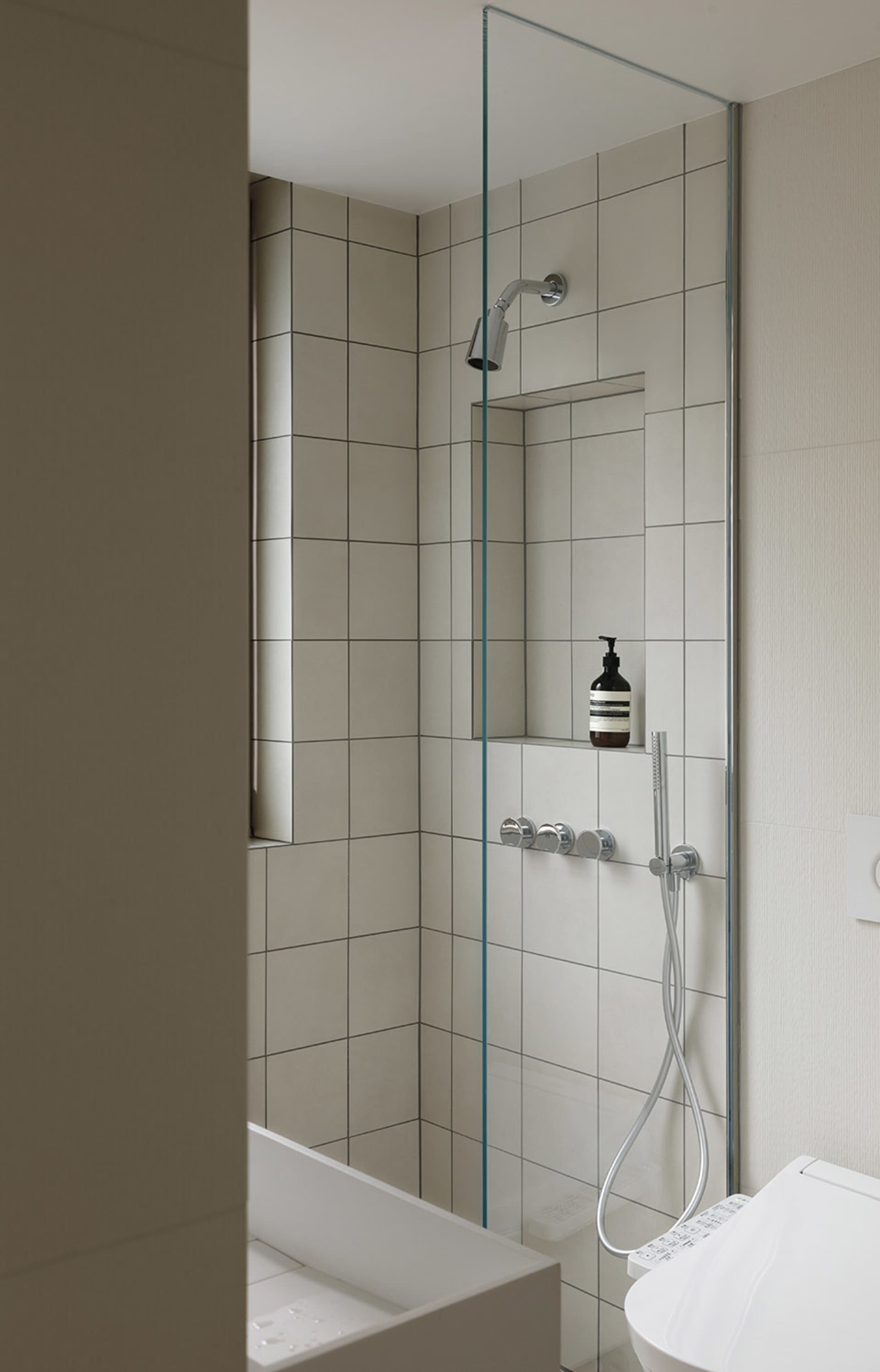 A modern bathroom featuring white tiled walls and a glass shower enclosure.
