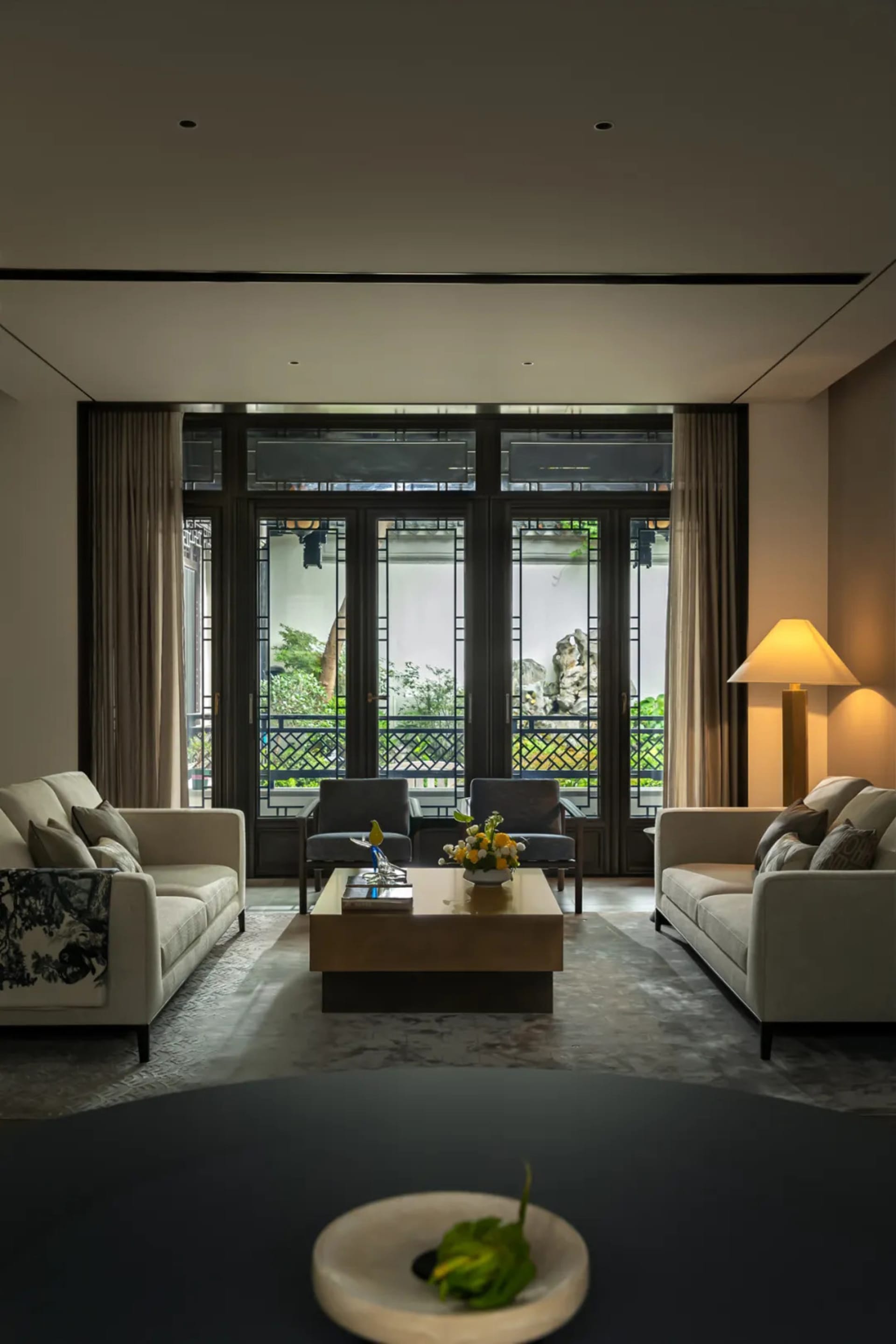 A modern living room featuring white sofas, dark wood coffee table, and floor lamp with yellow light.