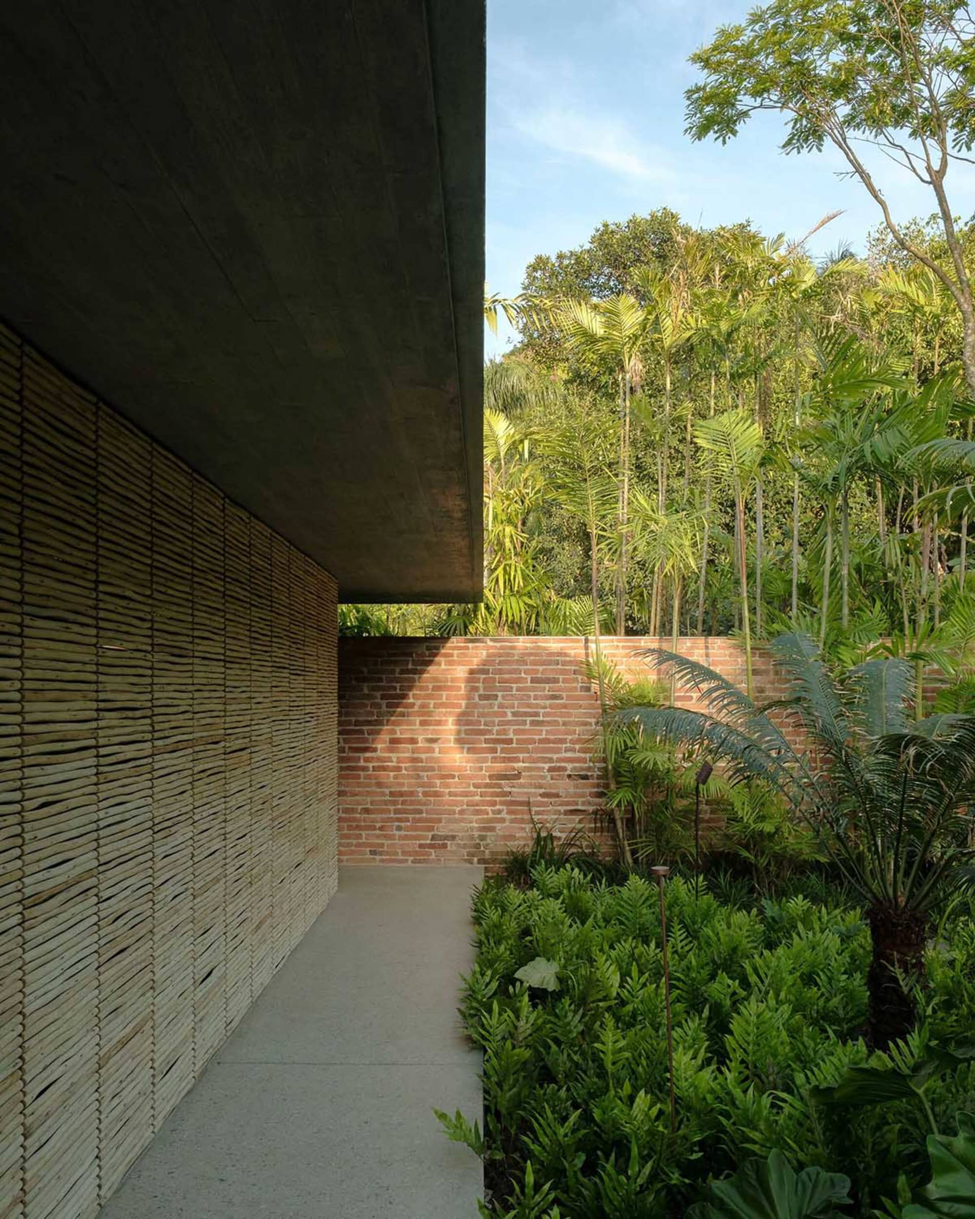 A walkway with bamboo walls and a brick wall, surrounded by lush greenery.