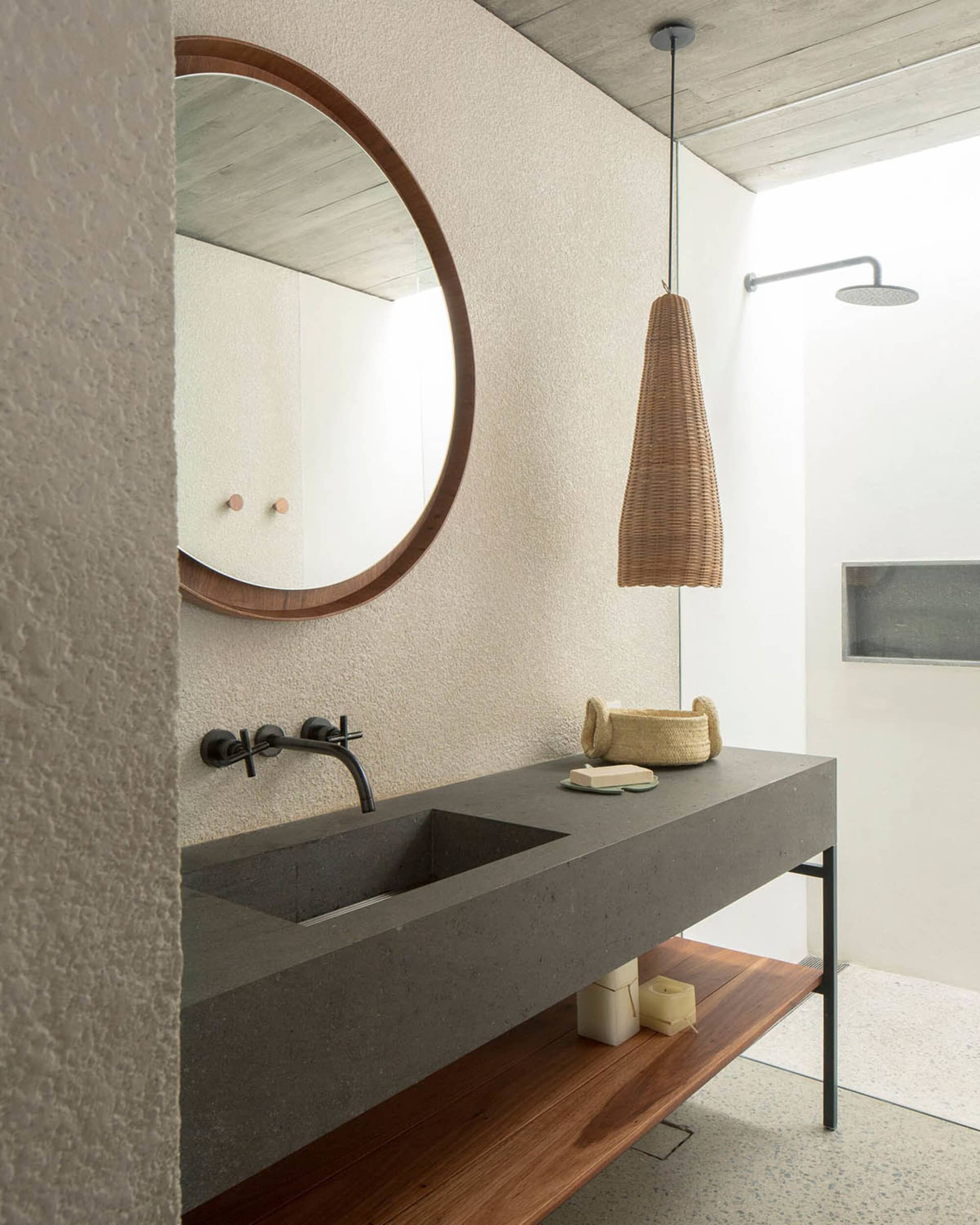 Modern minimalist bathroom with a concrete countertop and sink, featuring a wooden shelf below and a circular mirror above.