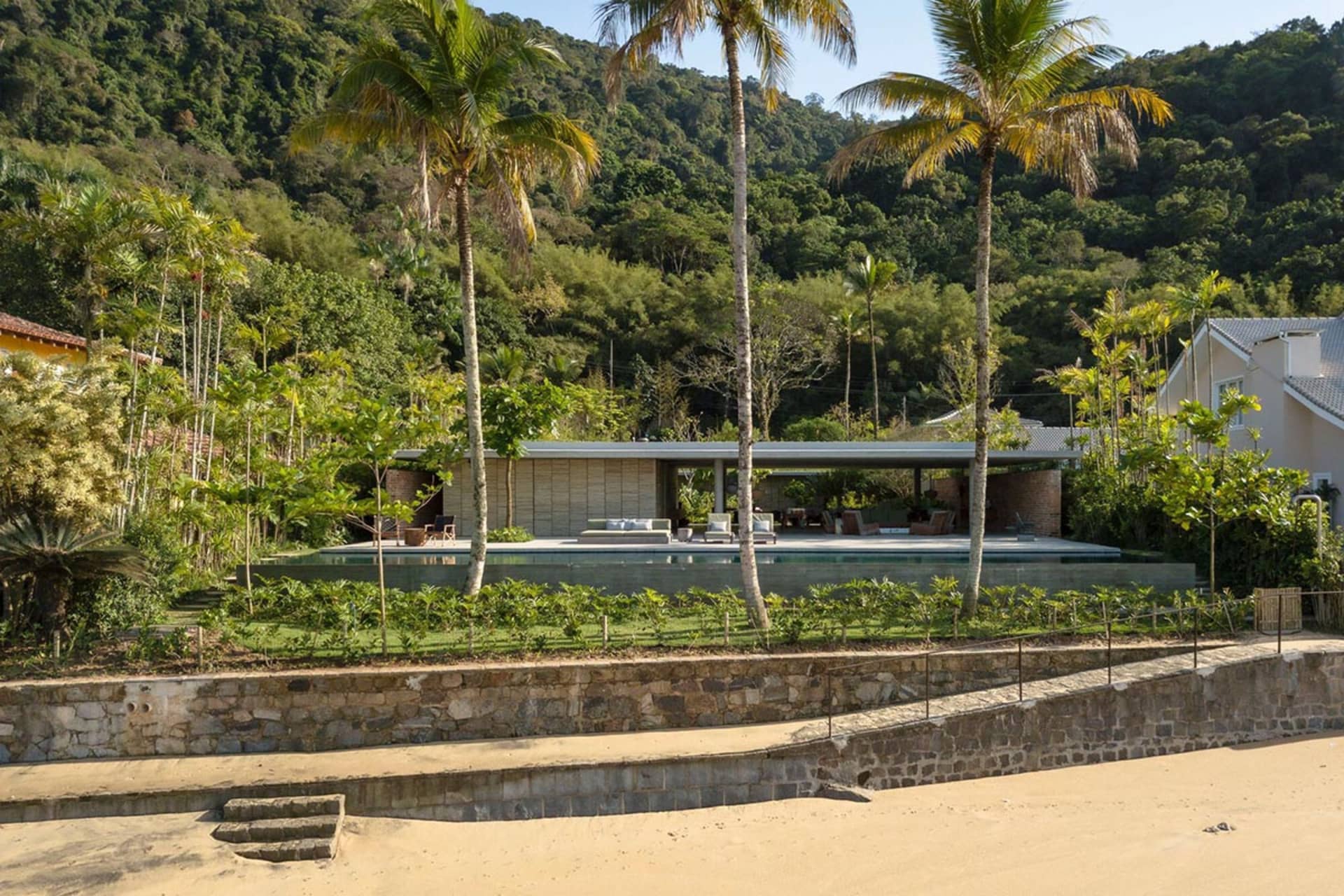 極簡住宅擁有混凝土牆面與大型玻璃牆，環繞著茂密綠意。