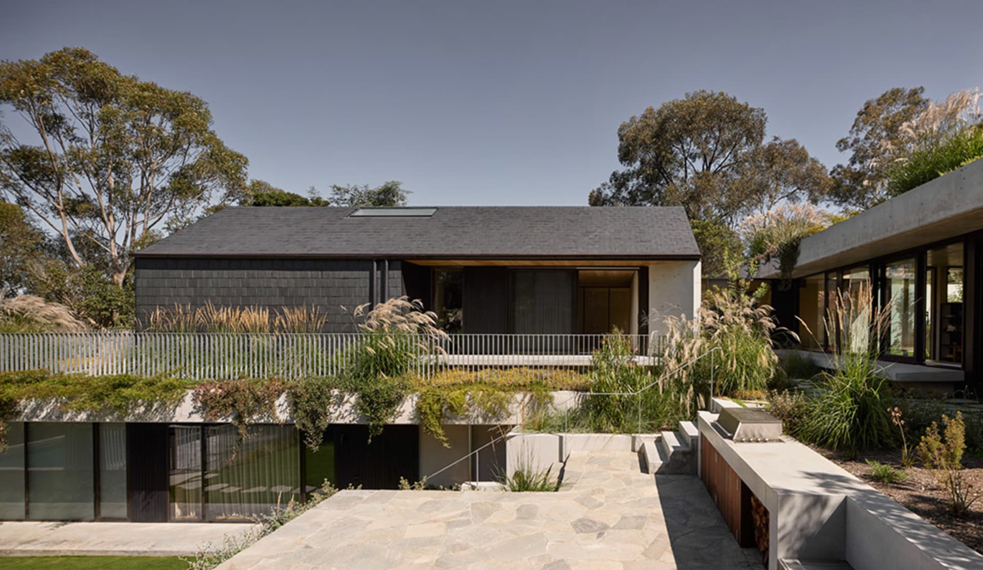 A modern residential exterior featuring concrete detailing, glass walls, and wood accents.