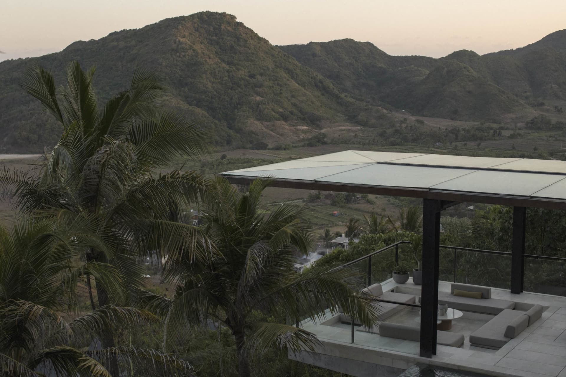 Modern residential terrace with concrete and glass structures surrounded by palm trees, overlooking scenic mountainous landsc