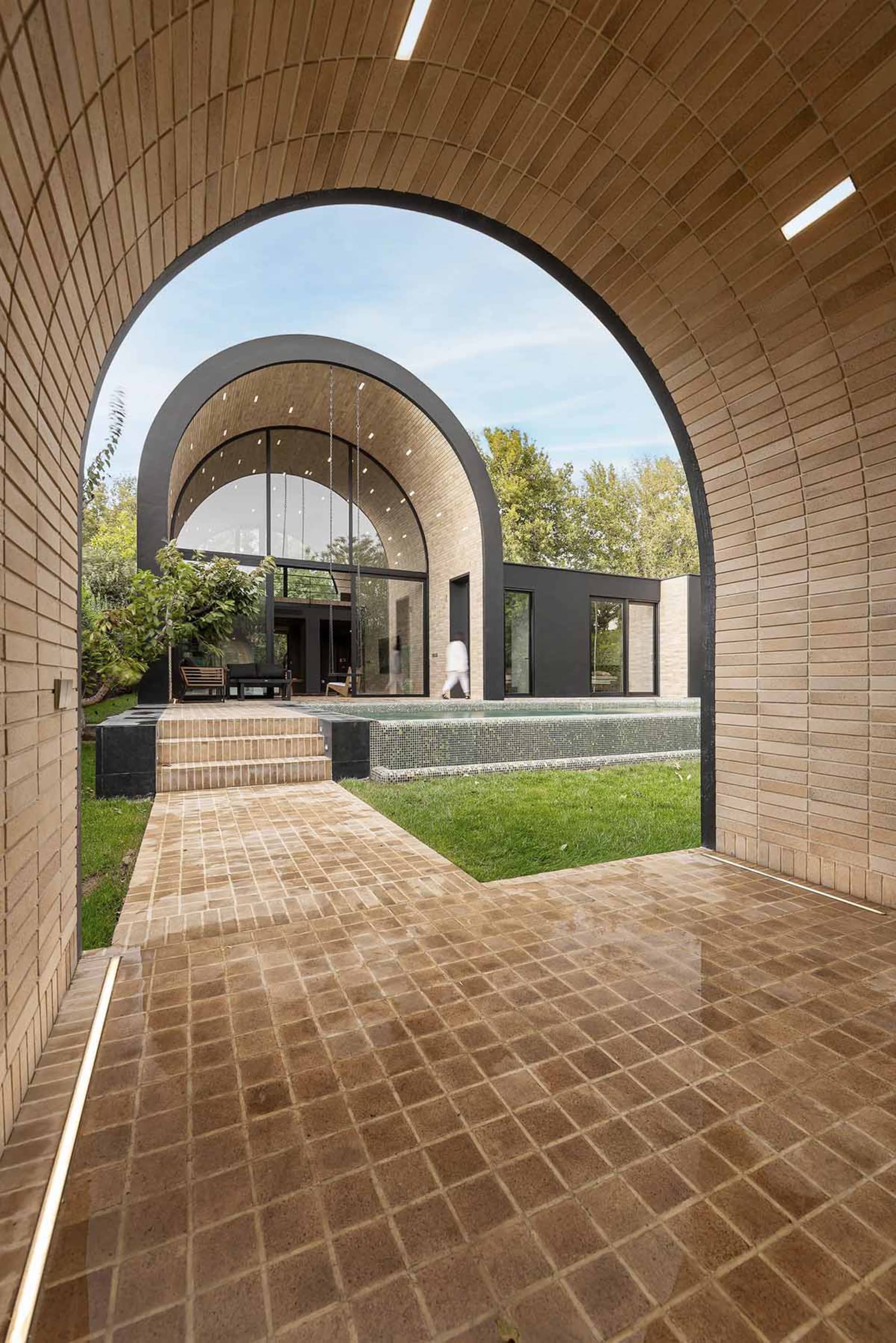 A modern architectural exterior featuring a brick walkway, concrete floor, and tiled poolside area.