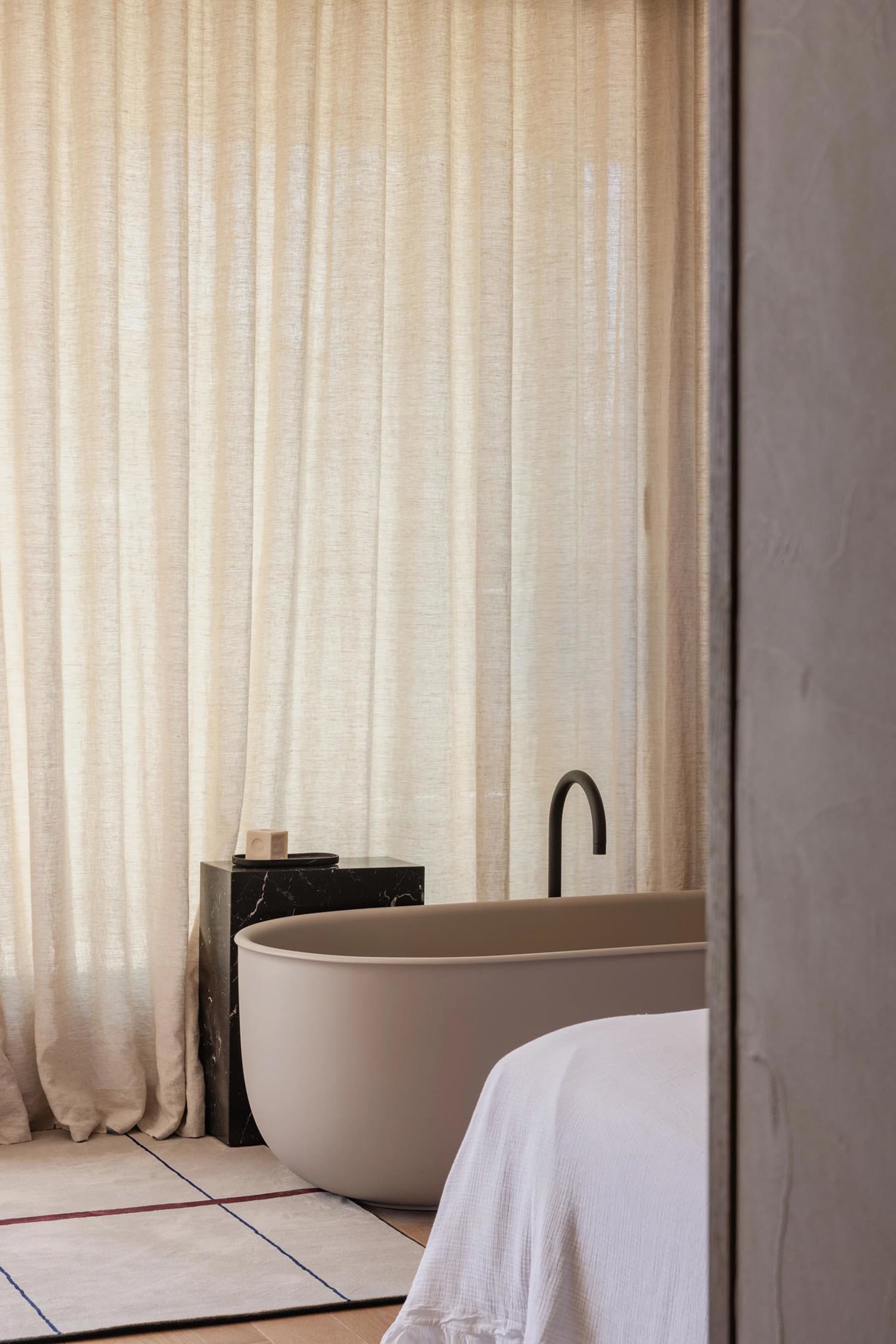Minimalist bathroom featuring a marble bathtub, linen curtains, and porcelain fixtures.