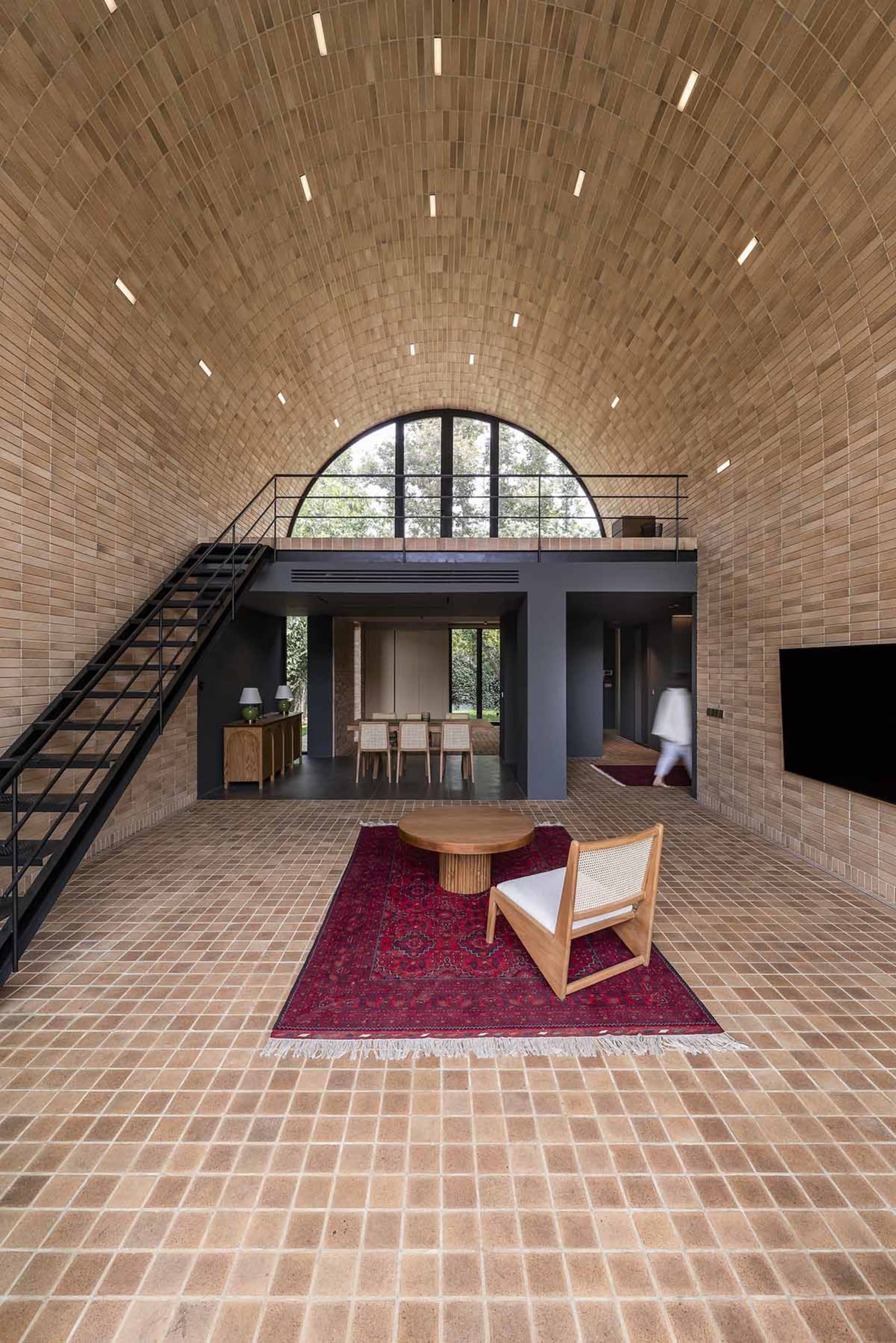 A modern living room with grey clay tiles on the floor and walls, featuring a large arched window and a wooden chair on a red
