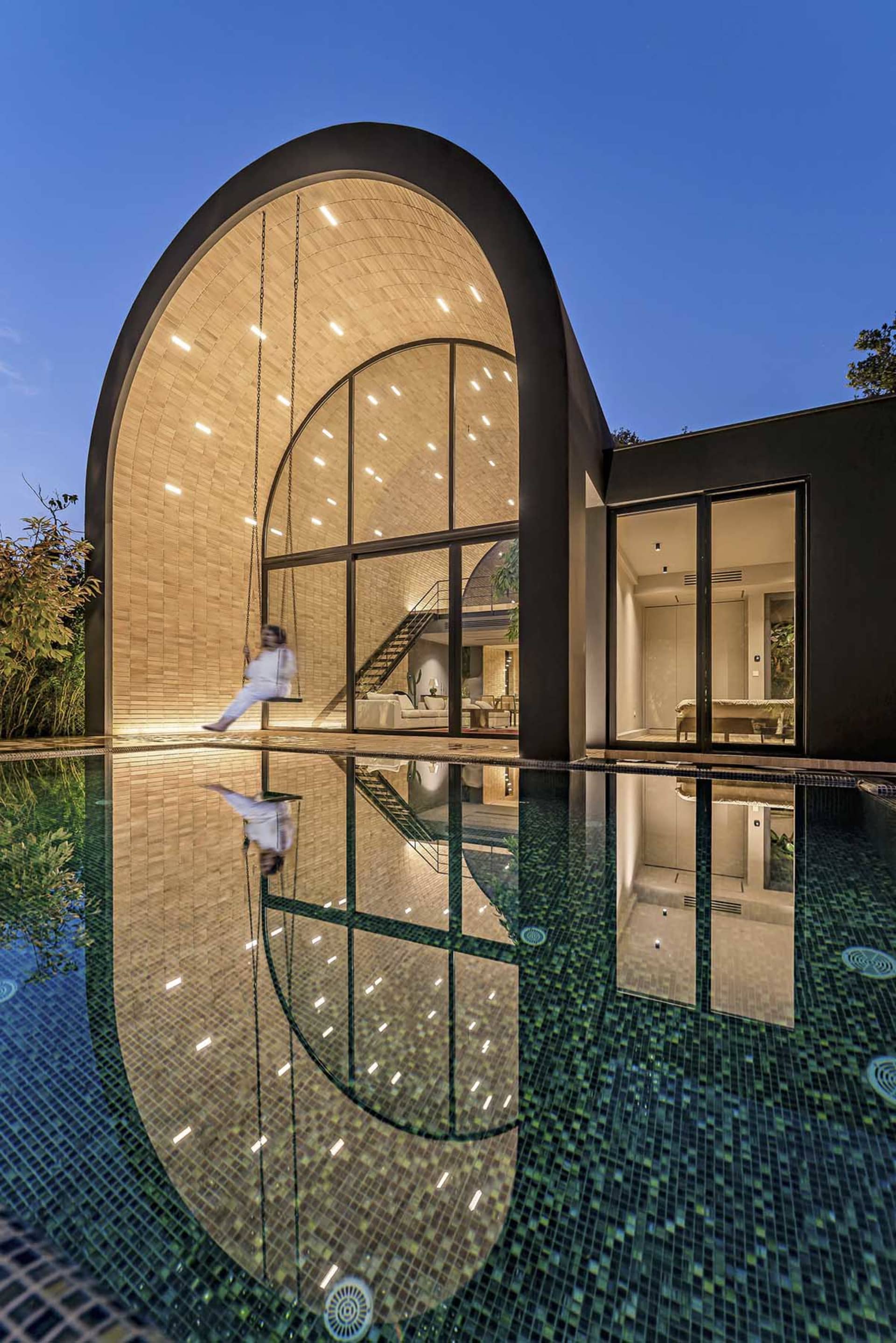 A modern minimalist house with a glass wall reflected in a swimming pool.