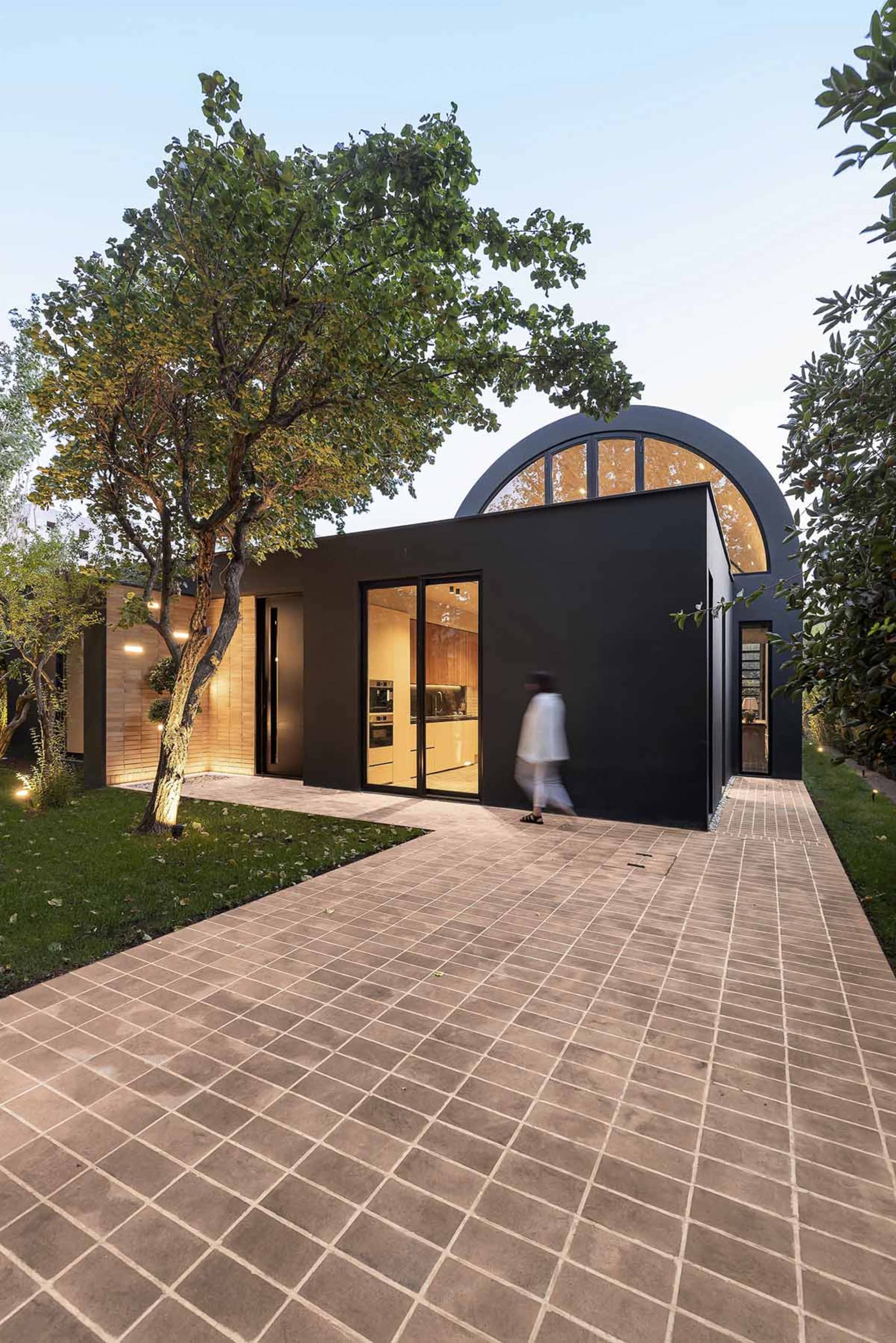A modern residential house with a black exterior and large windows, surrounded by greenery.