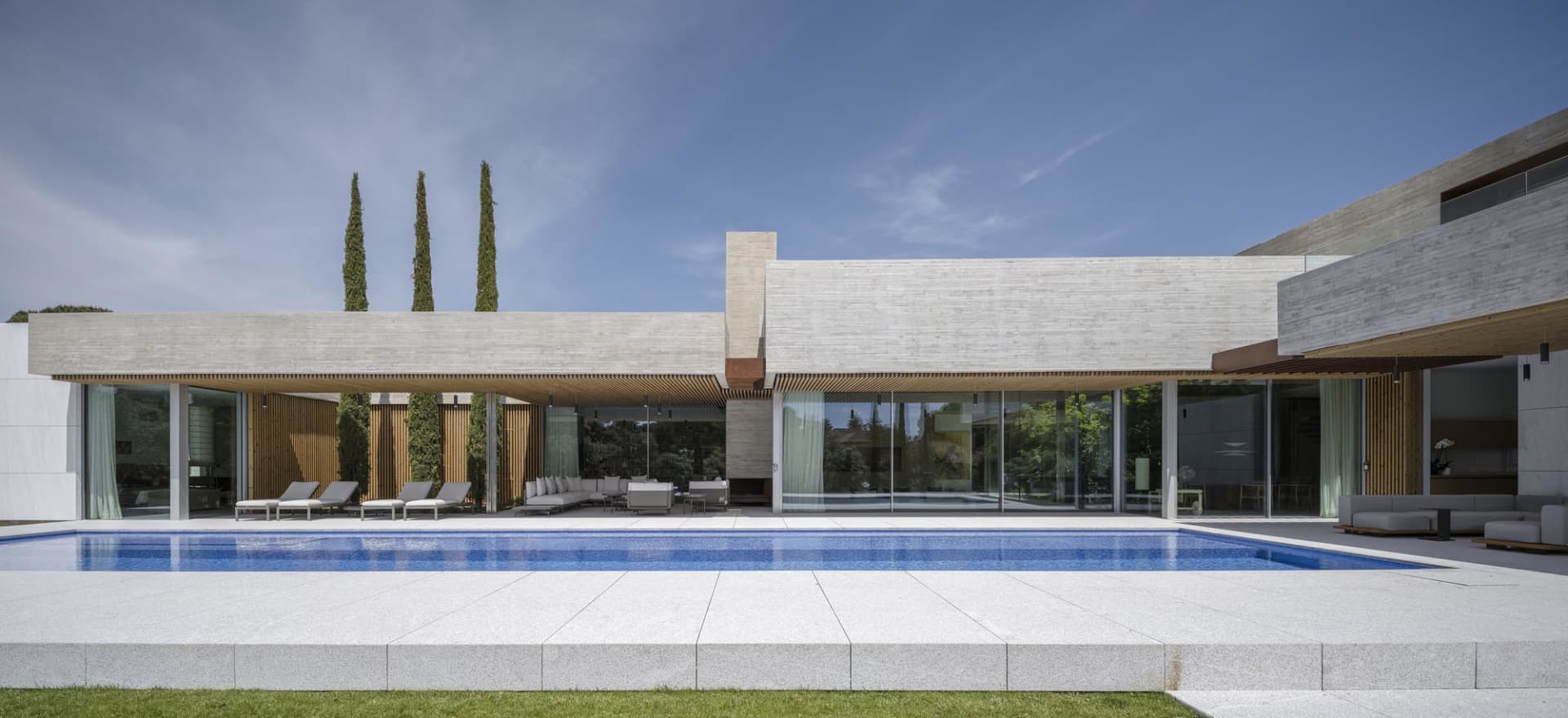 Modern residential exterior with a concrete facade and a swimming pool surrounded by a patio with an outdoor seating area.