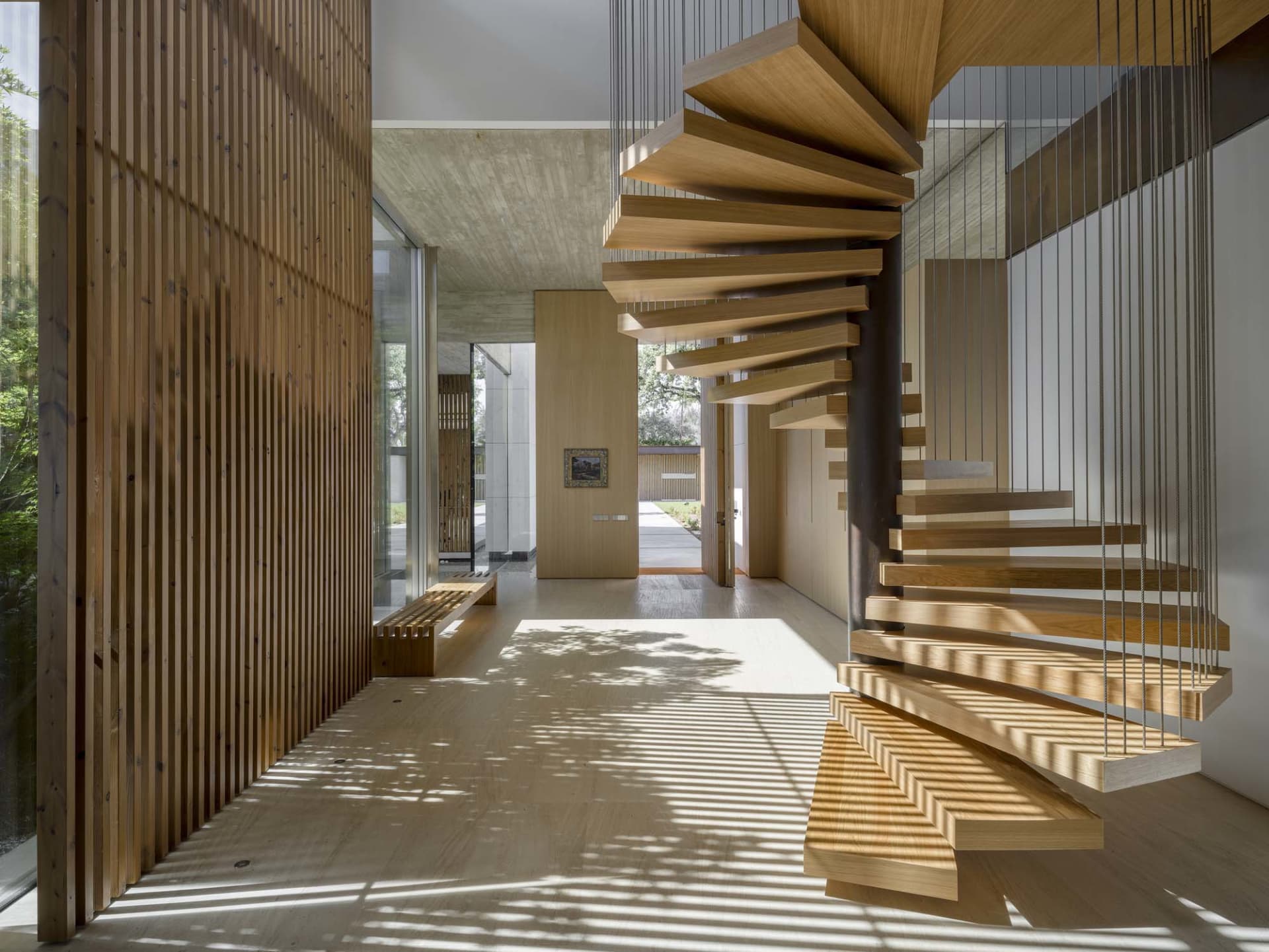 A modern floating staircase with wooden steps and cables hanging from the ceiling.