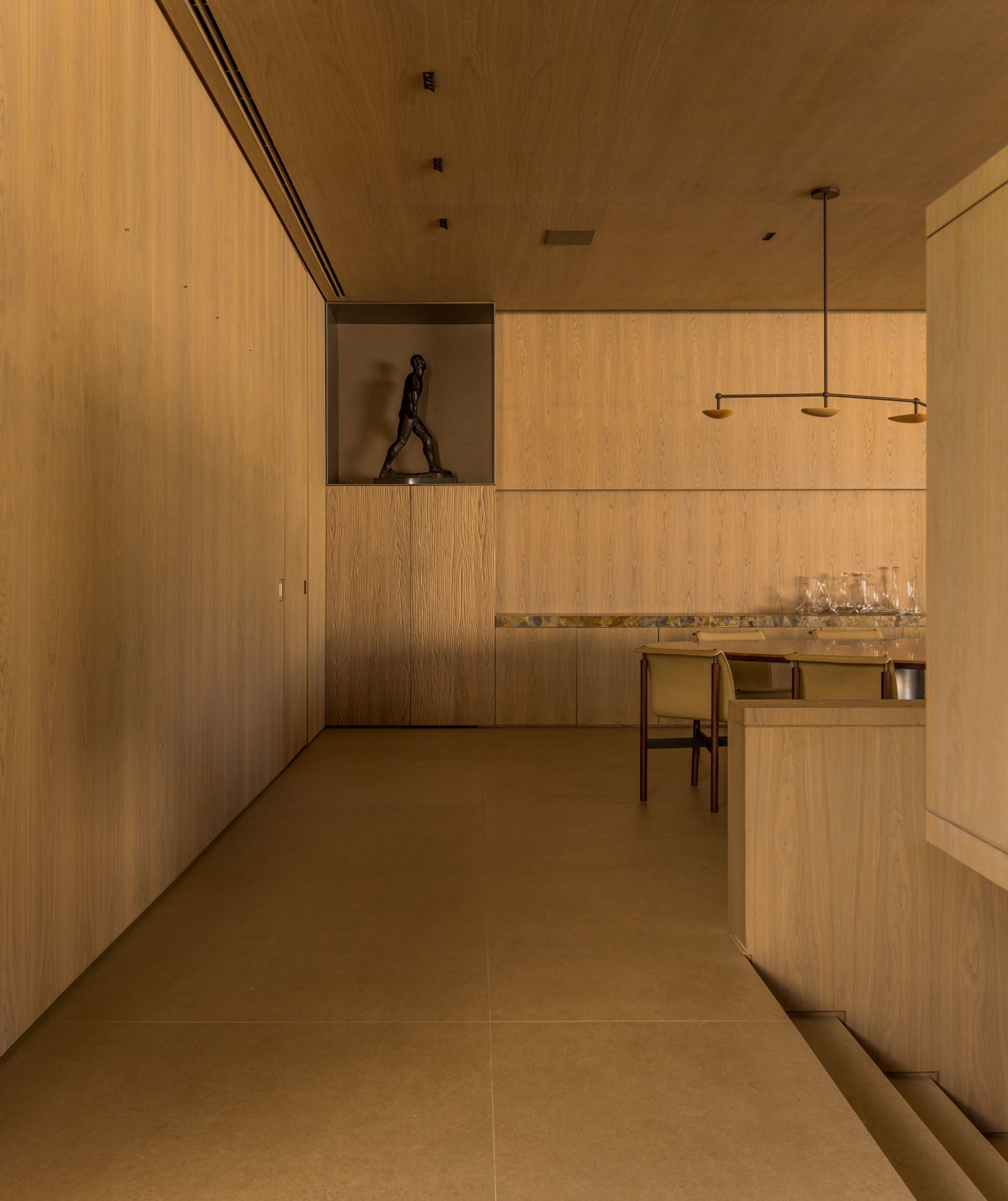 A modern, minimalist kitchen with wooden walls and flooring, featuring a dining table and chairs, and a sculpture on the wall