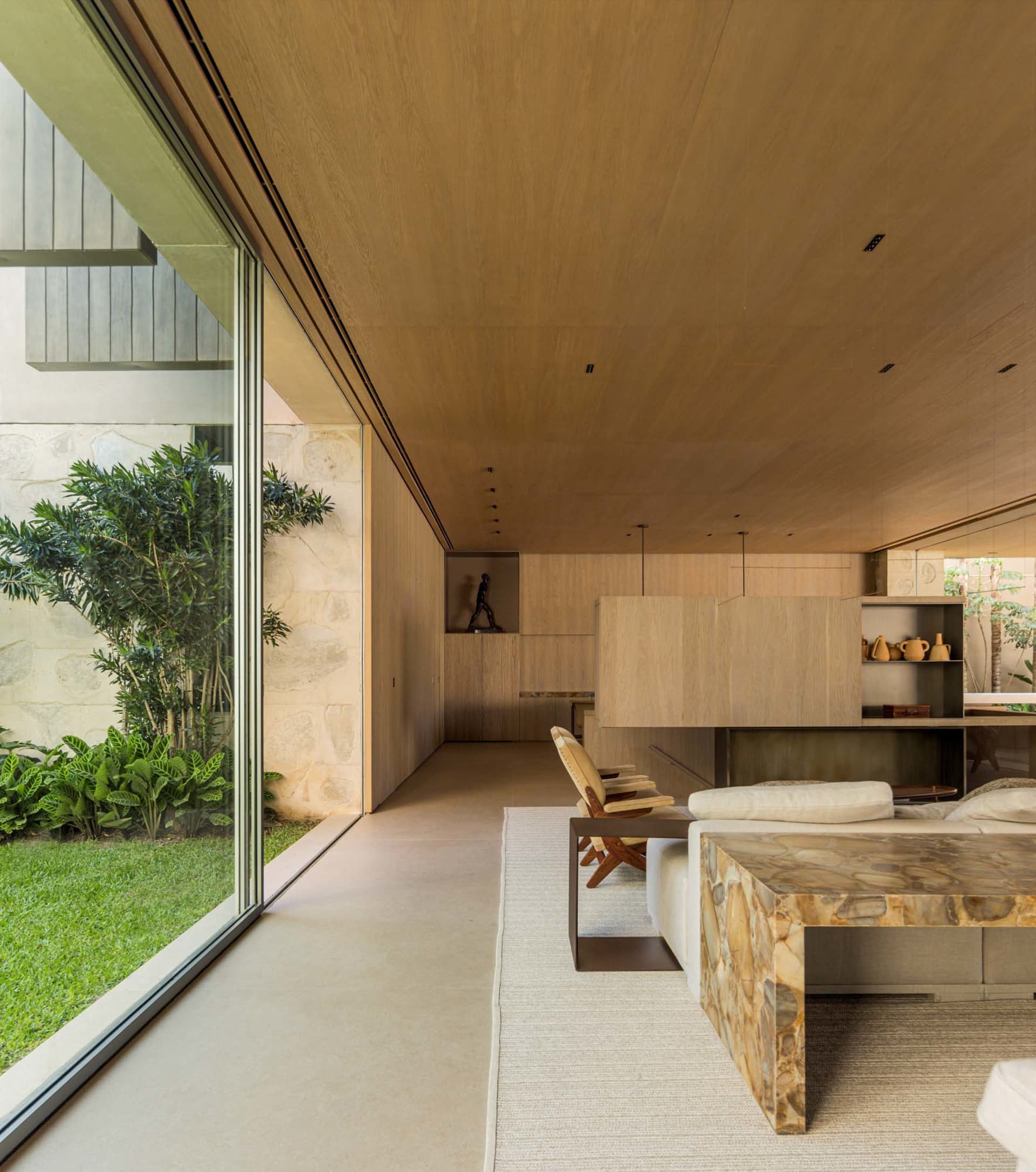 Modern minimalist living room featuring wooden walls, stone furniture, and a large glass window with greenery outside.