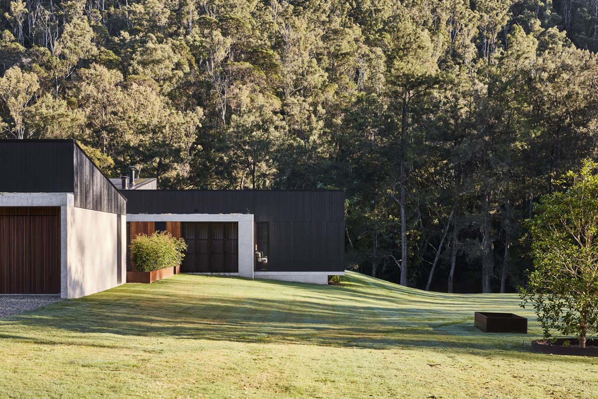 Modern home exterior with concrete and wooden features surrounded by greenery.