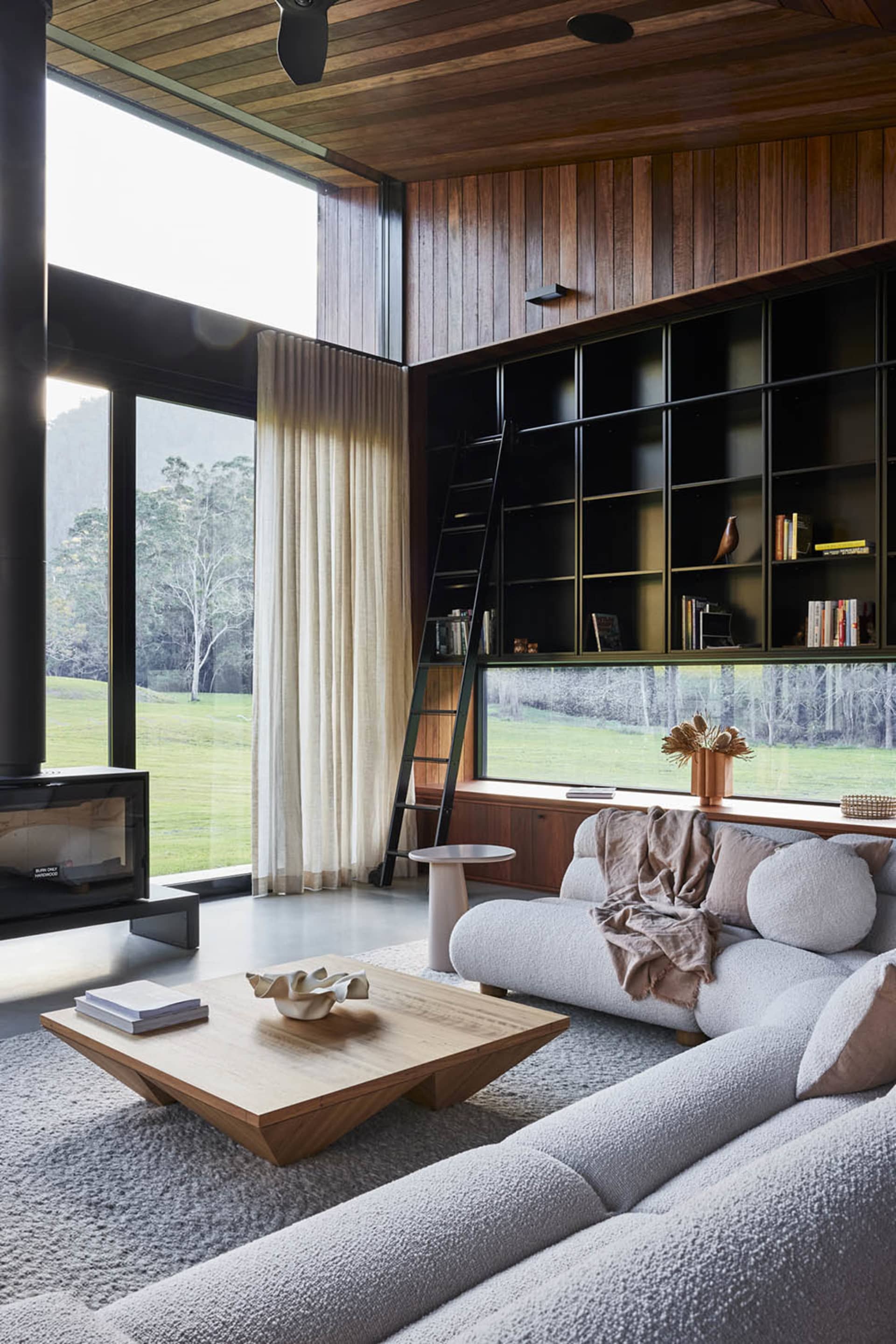 A modern living room with large windows, a wooden coffee table, and a comfortable sofa.