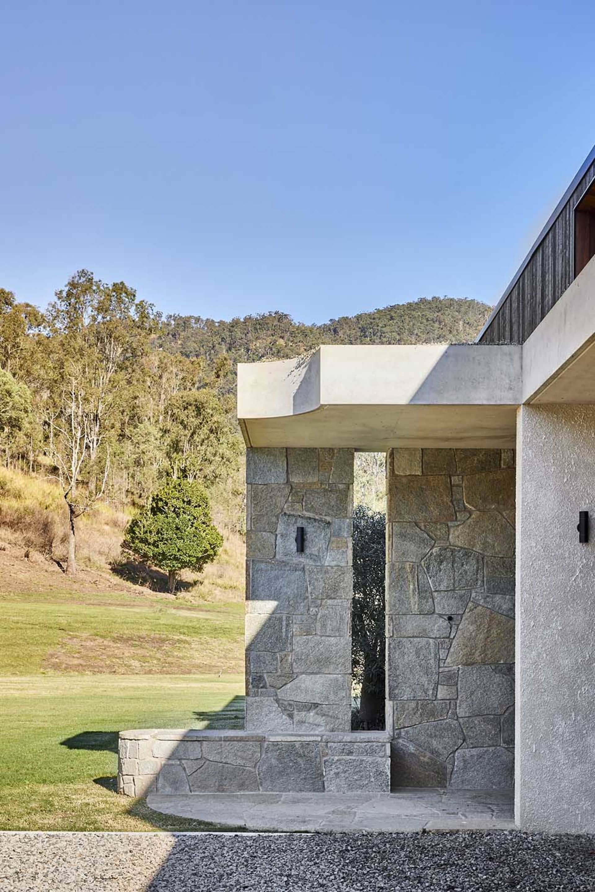 Modern residential exterior with granite entryway, landscaped yard, and mountainous backdrop.