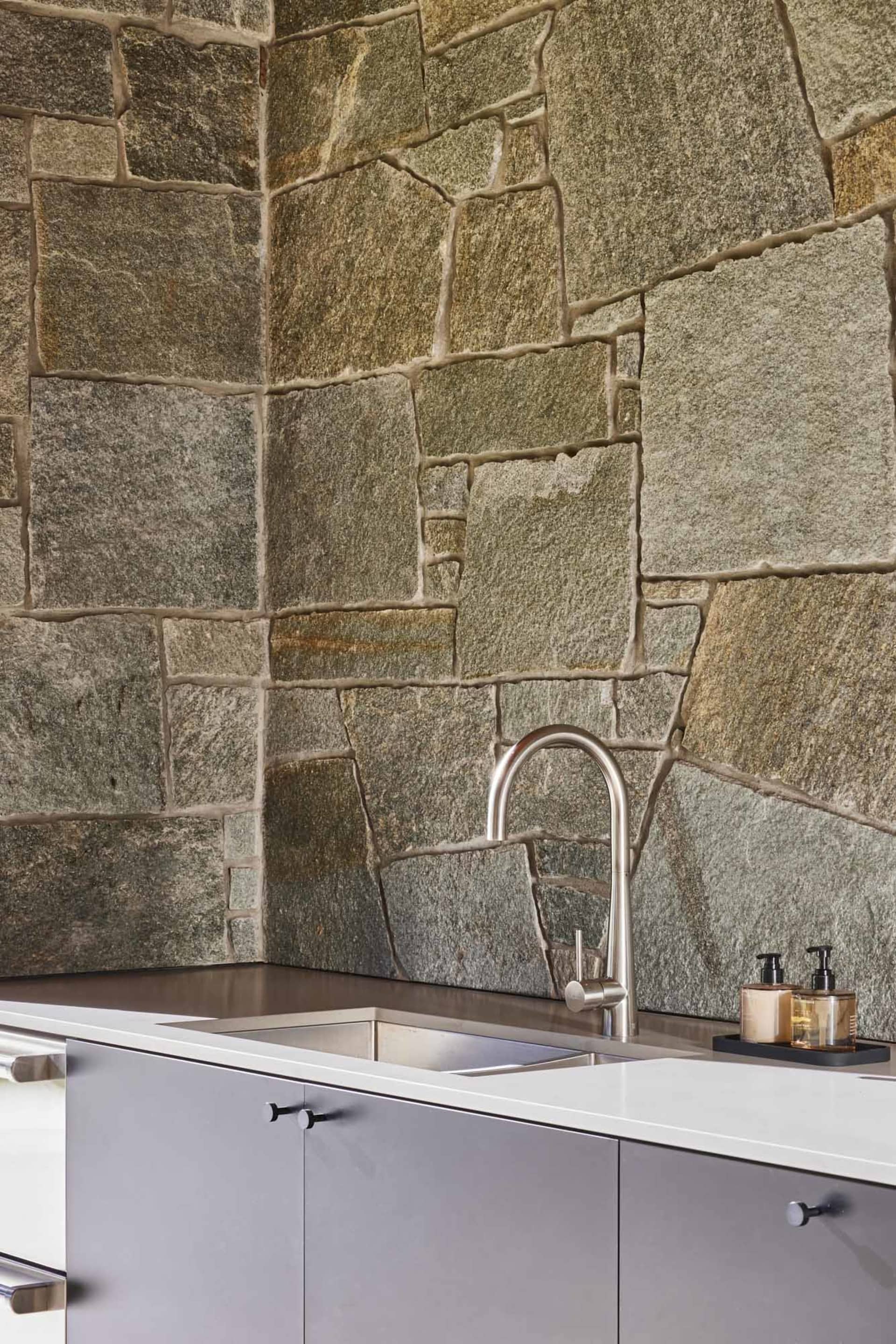A modern kitchen with a stone wall and stainless steel faucet