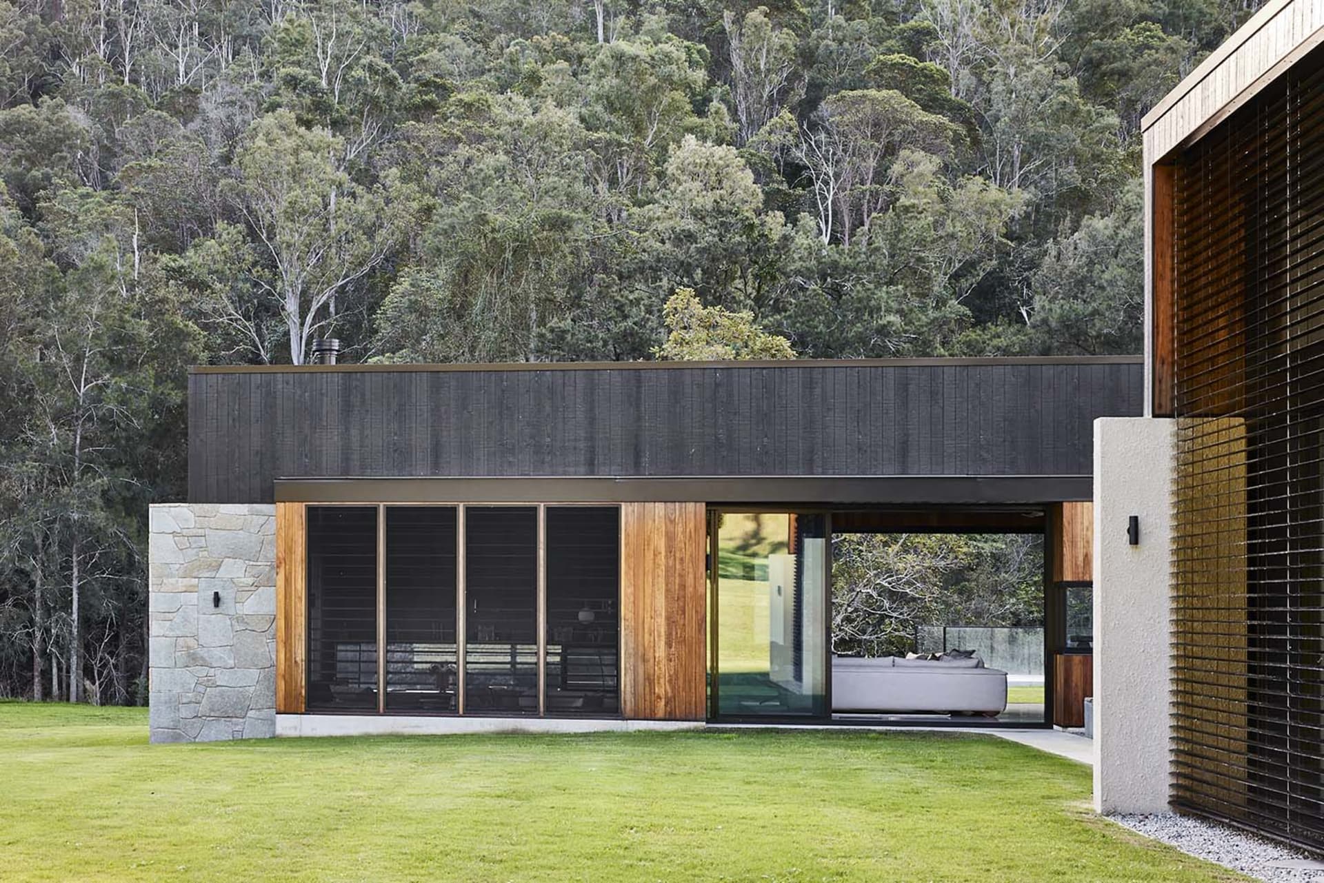 A modern residential exterior featuring wooden panels, glass doors, and stone accents.