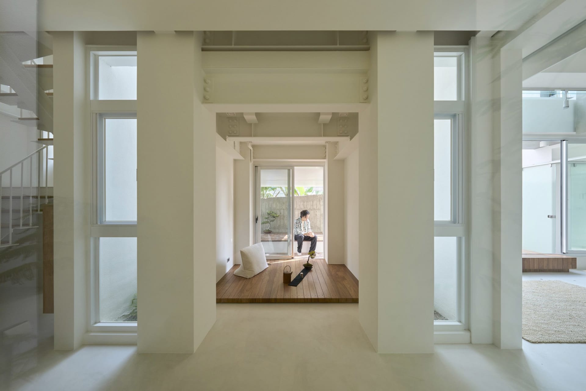A minimalist interior space with white walls, wood flooring, and a concrete structure.