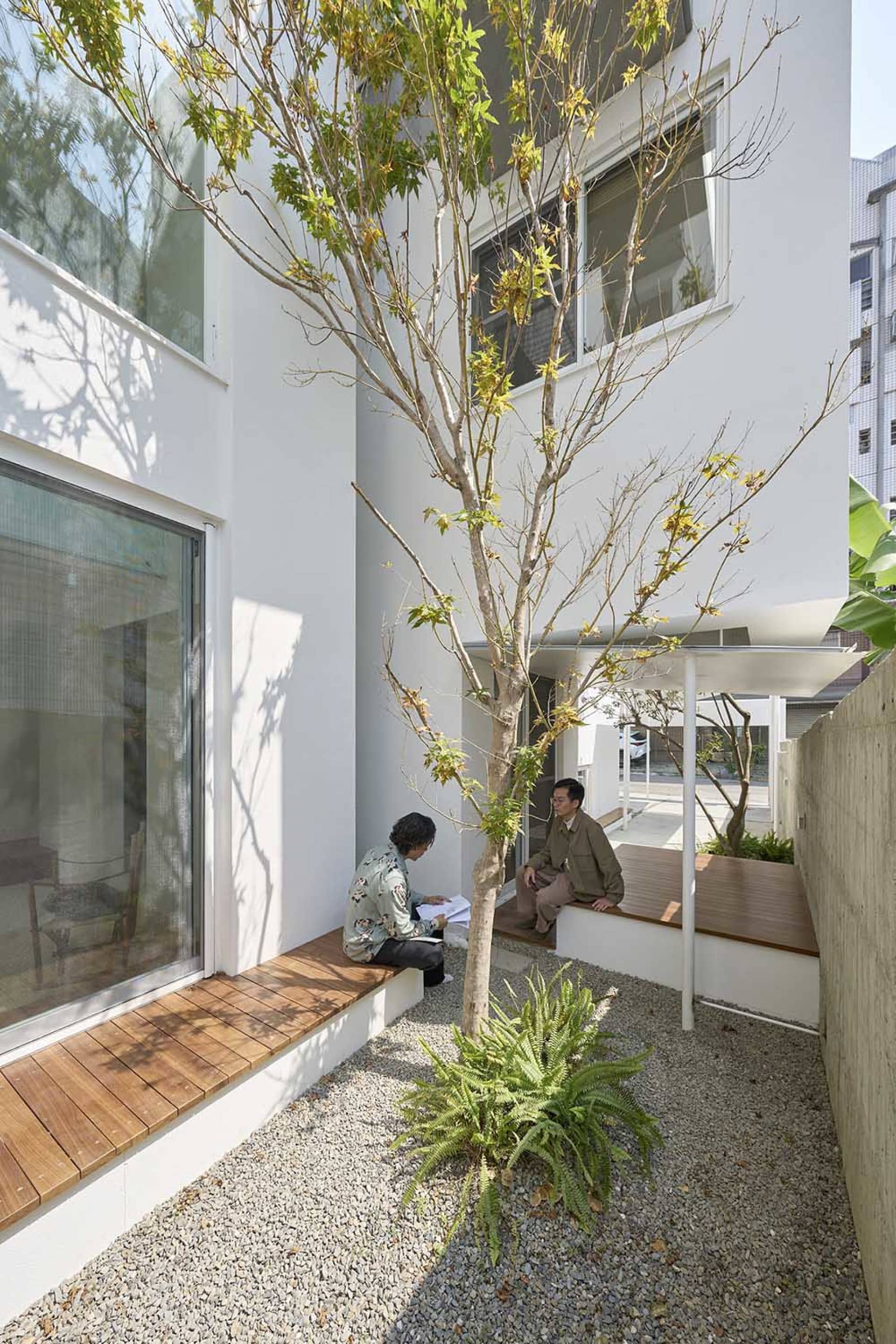 Minimalist residential outdoor space featuring concrete and wood materials, with two individuals sitting on benches surrounde