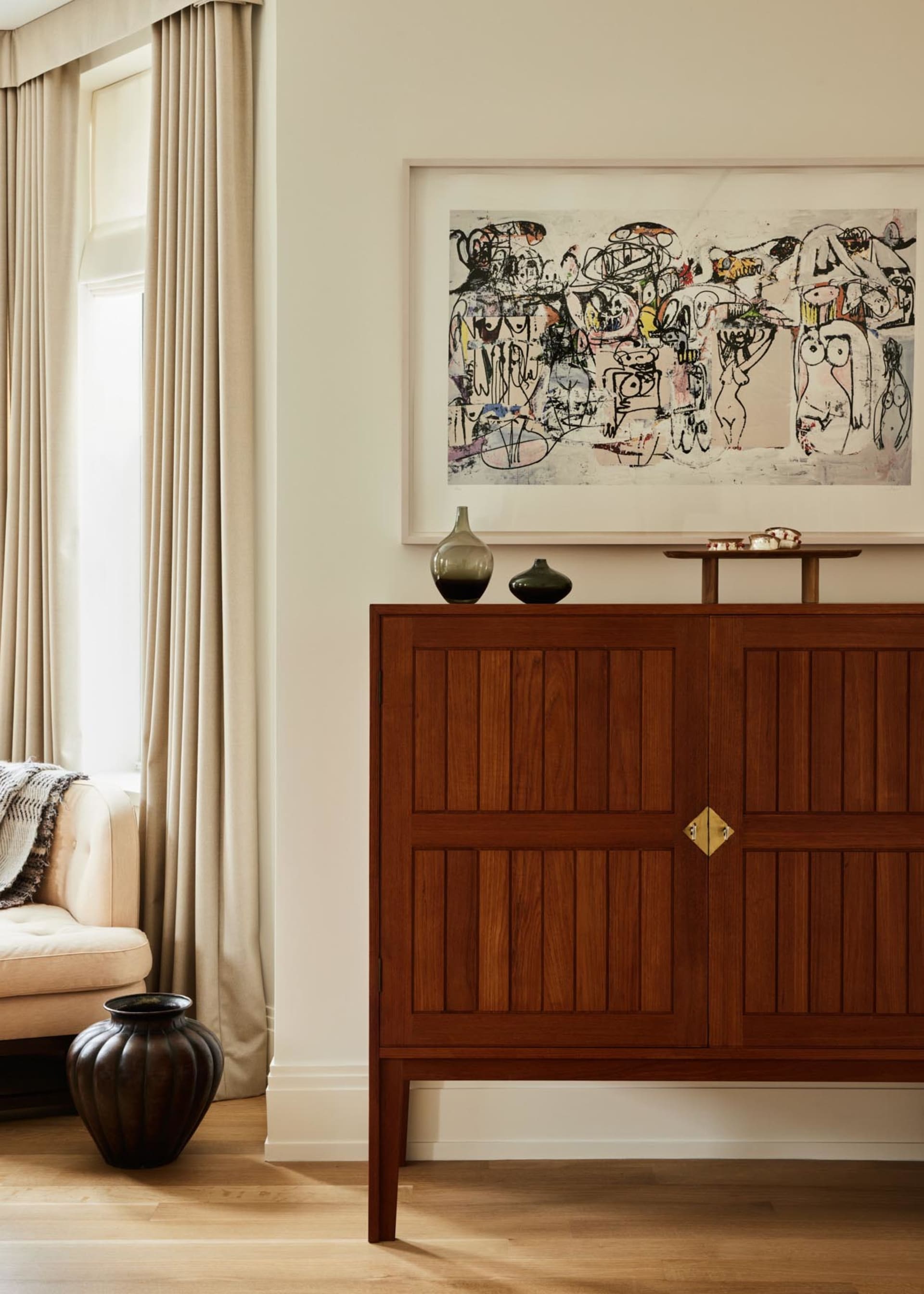 Modern living room featuring a wooden cabinet with artwork on the wall and a comfortable seating area by the window.