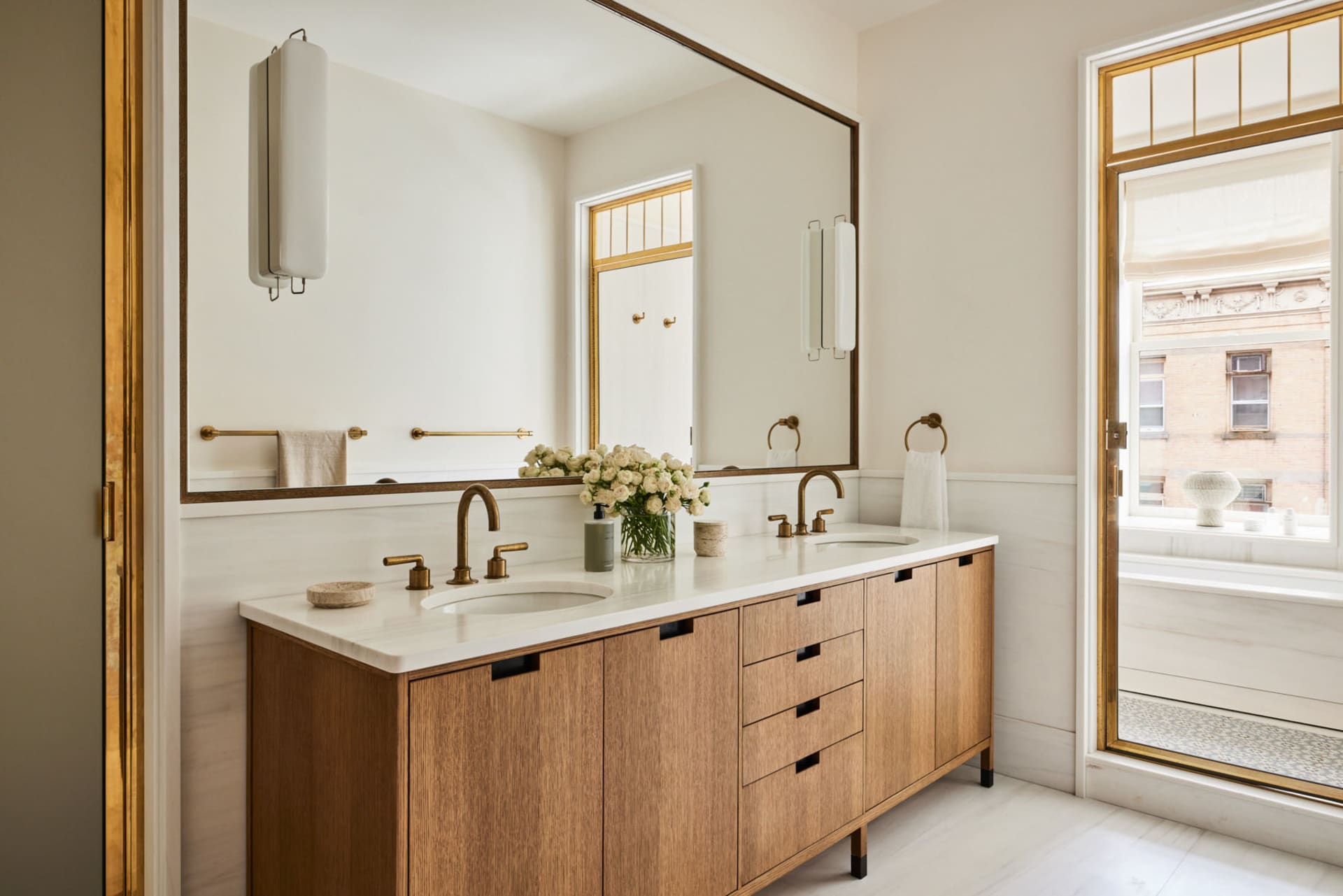 A modern bathroom featuring a marble countertop, oak cabinets, and brass fittings.