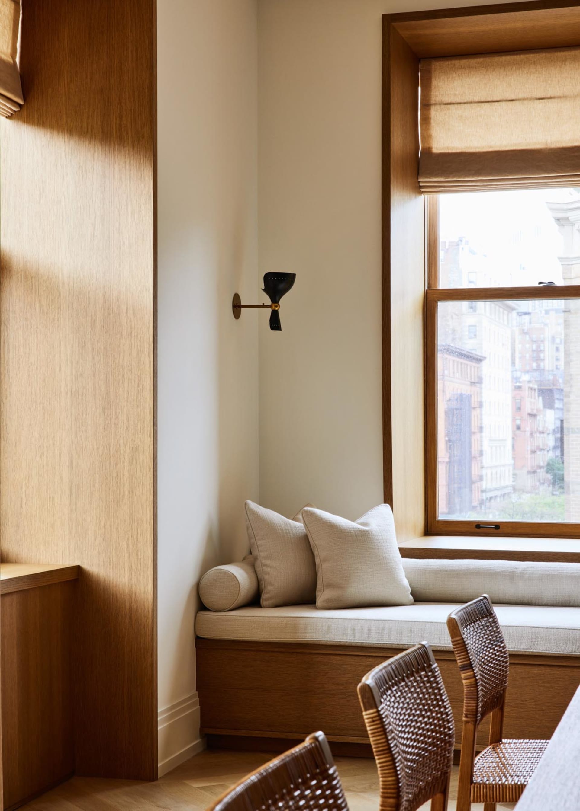 Modern residential space featuring comfortable seating with wooden cushions and a window with light filtering through blinds.