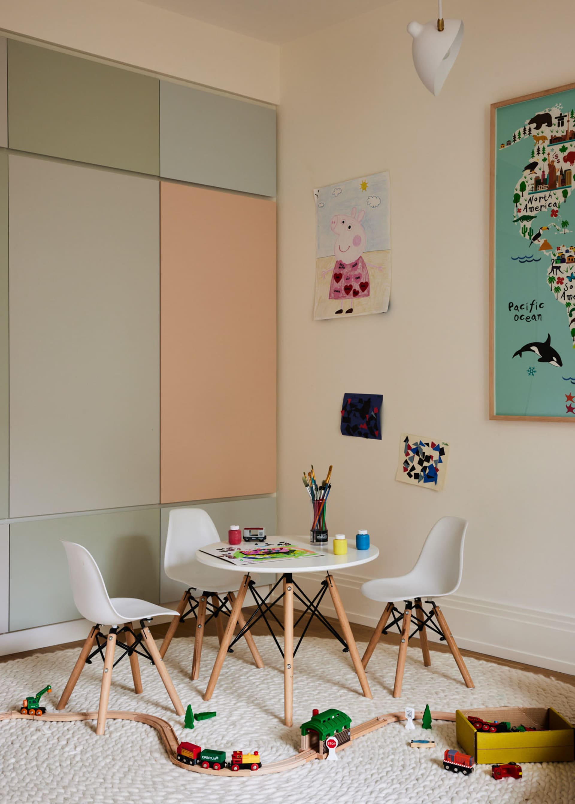 A modern playroom with wooden furniture and toys on the floor, featuring a small table with art supplies and white chairs.