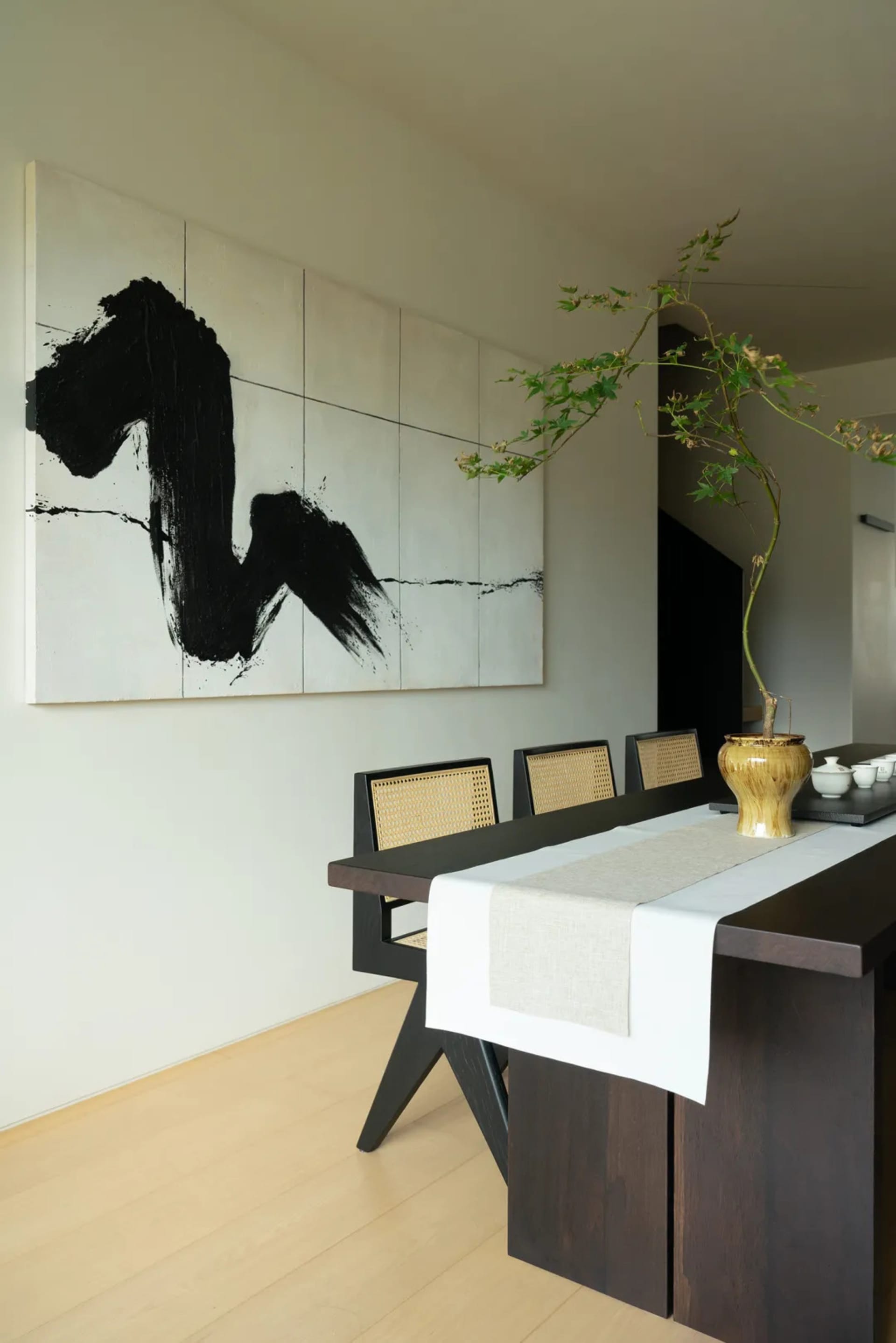 Minimalist dining room featuring wooden furniture and a black and white abstract painting on the wall.