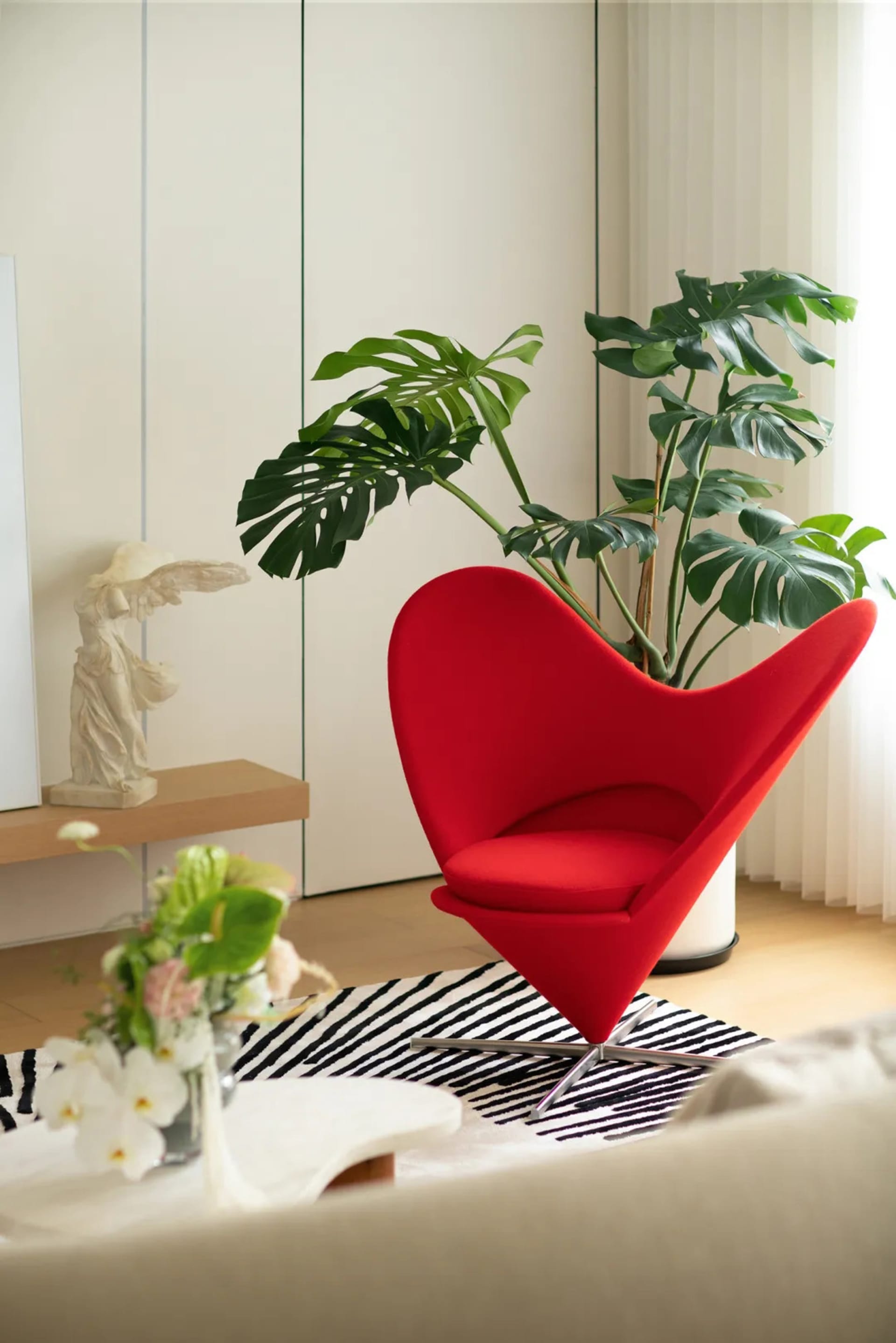 Modern living room featuring a red cone-shaped chair and a large green potted plant.