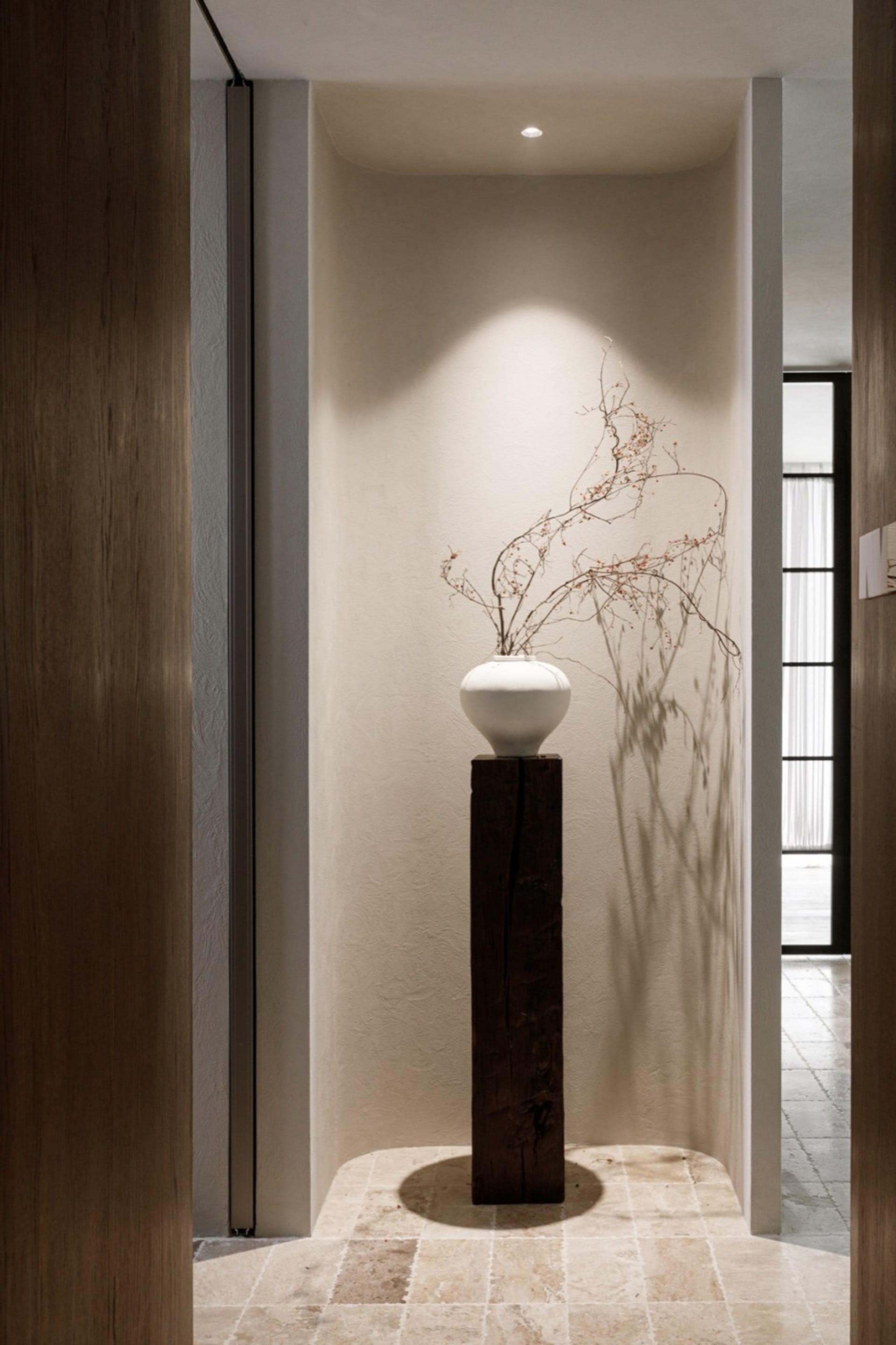 Ceramic vase with dried branches on a wooden pedestal in a minimalist interior design space.